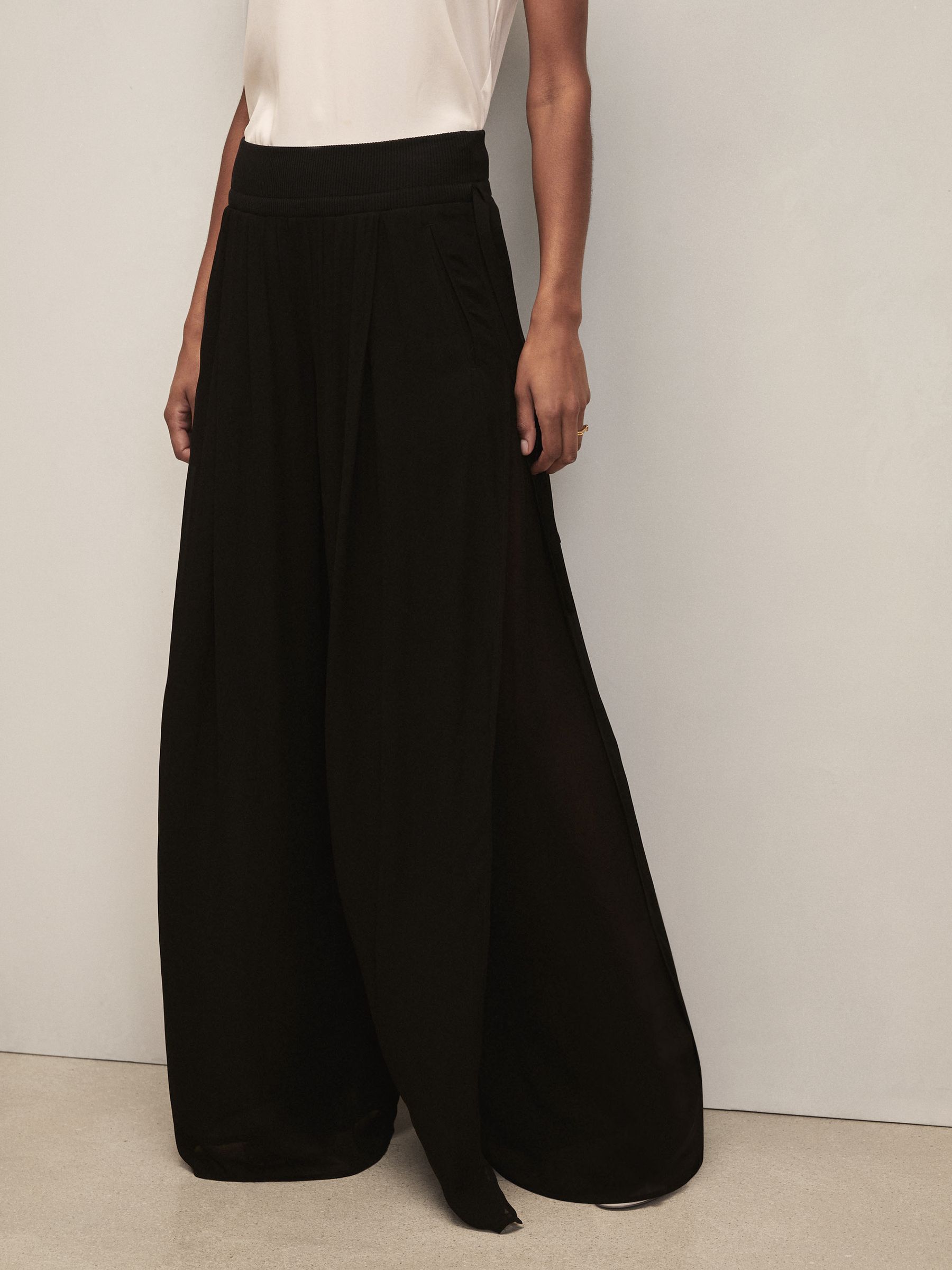 A pair of black chiffon wide-leg trousers with a waistband, side pockets, and a side slit in the top layer.