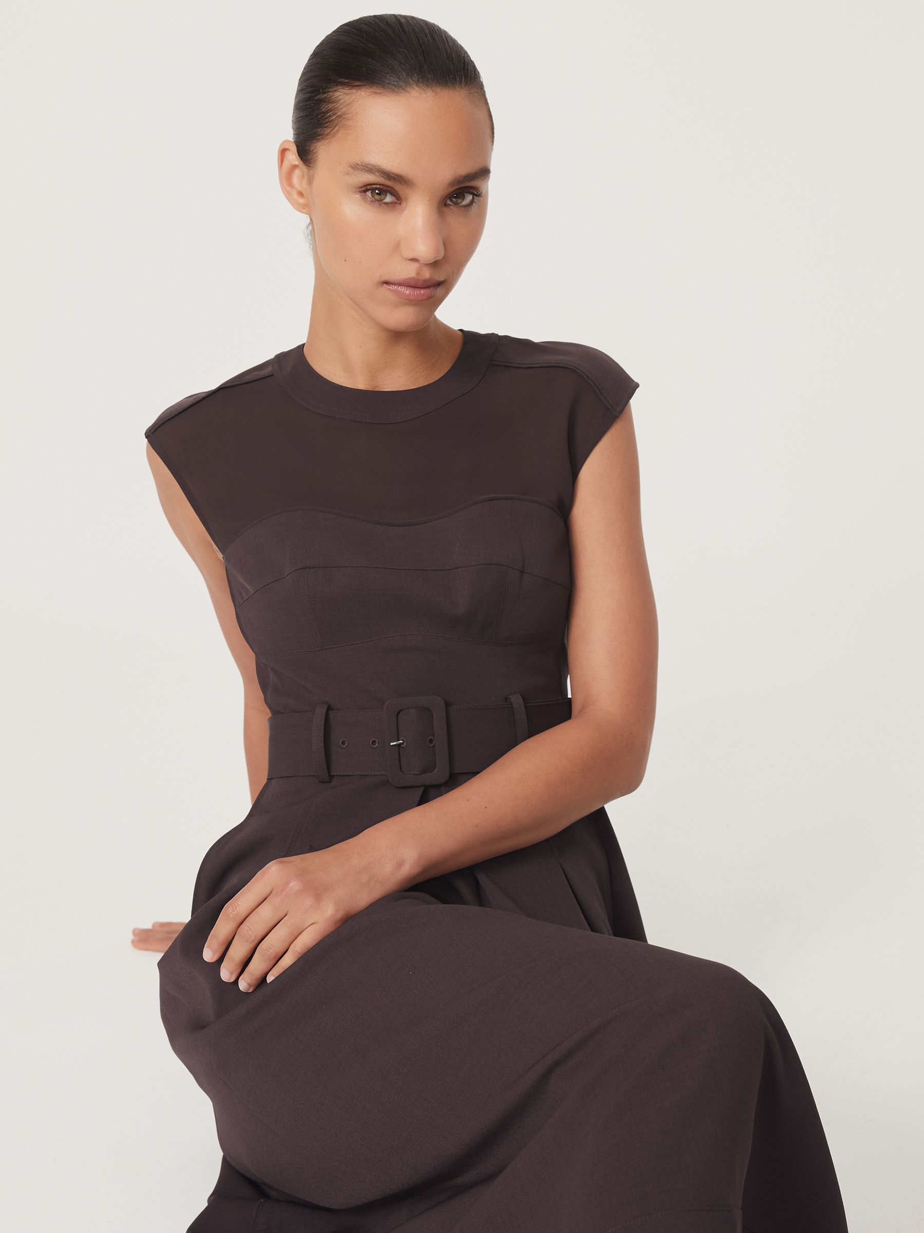 A woman wearing a burgundy midi dress with mesh panels, a high neckline, a belted waist, and a pleated skirt.