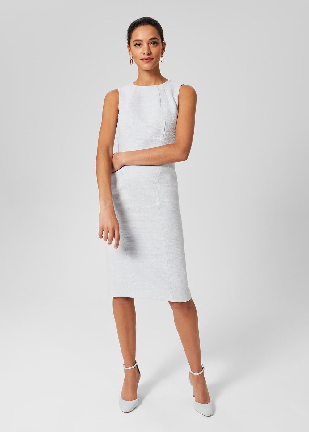 A woman wearing a white sleeveless shift dress with a crew neckline, standing against a plain background.