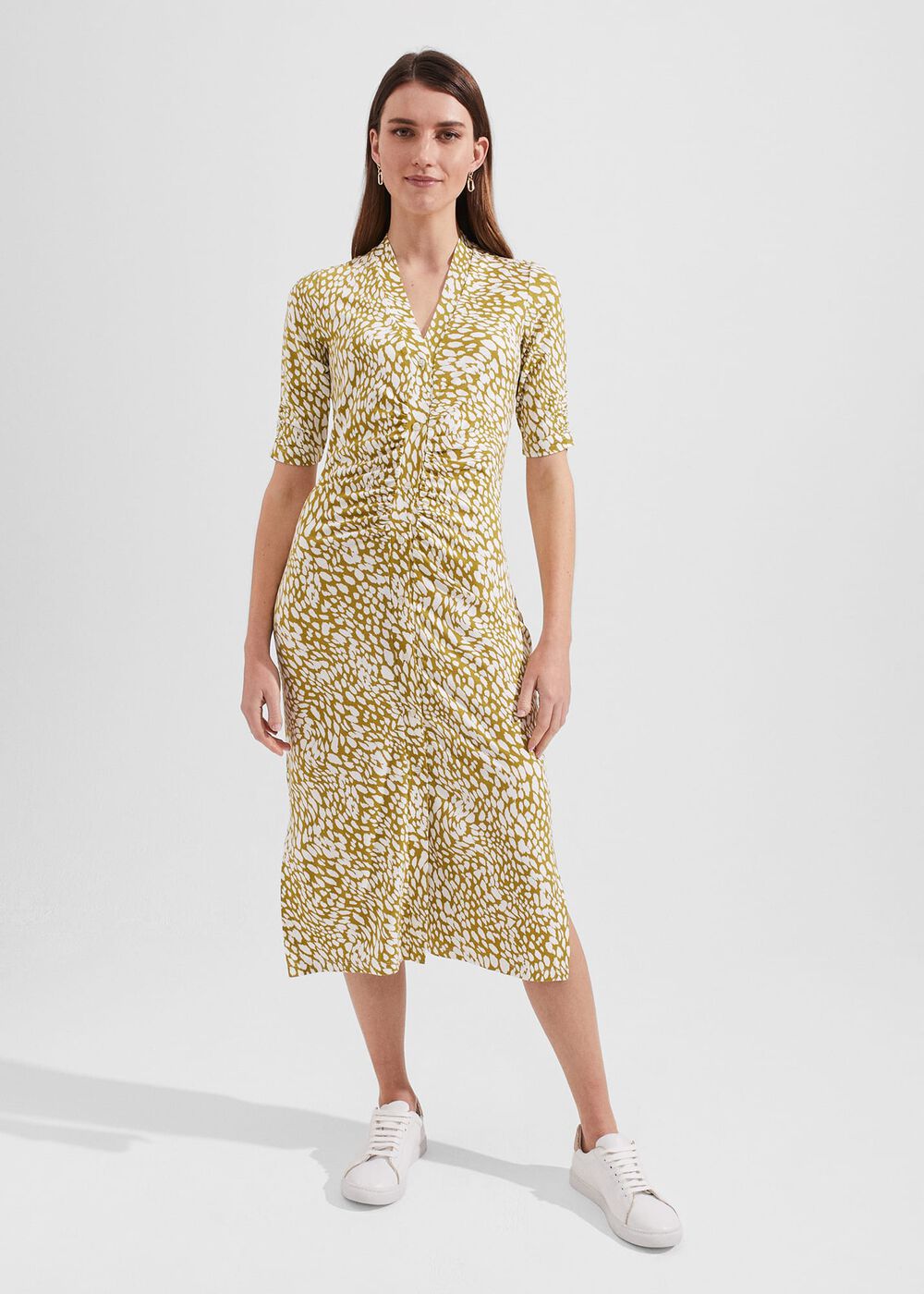 A woman wearing a yellow and white animal print midi dress with elbow-length sleeves and a fitted silhouette.