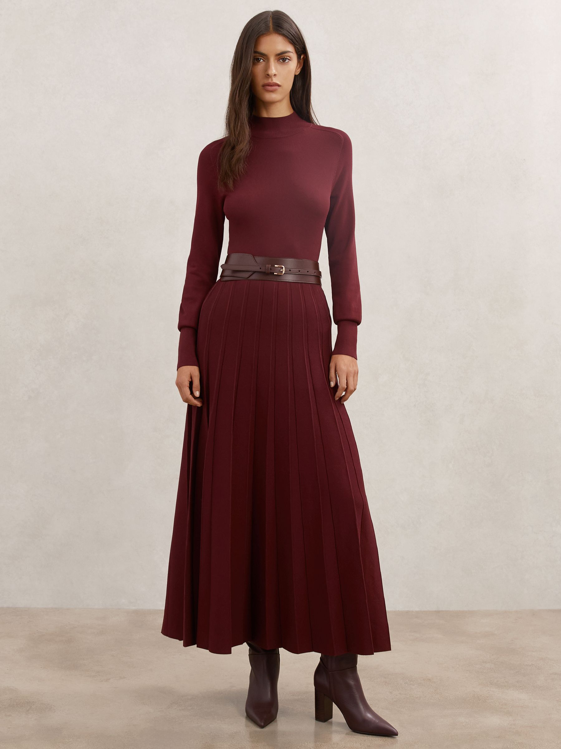 A woman wearing a Raspberry Red belted knit pleated midi dress with a high neckline and long sleeves.