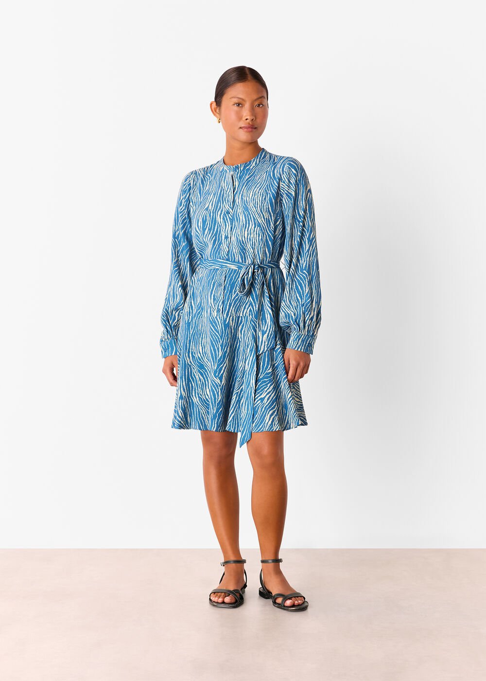 A woman wearing a blue and white zebra patterned mini dress with long sleeves, a round collar, and a tie belt at the waist.
