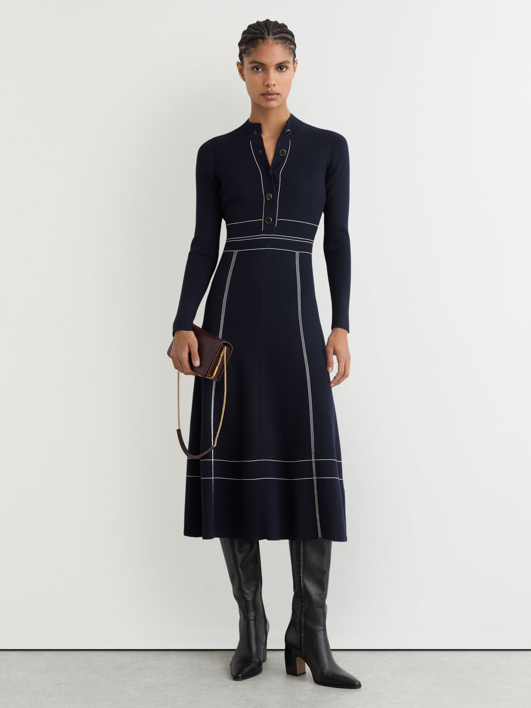 A woman wearing a navy knitted midi dress with contrast stitching, high neckline, and a half-button placket.