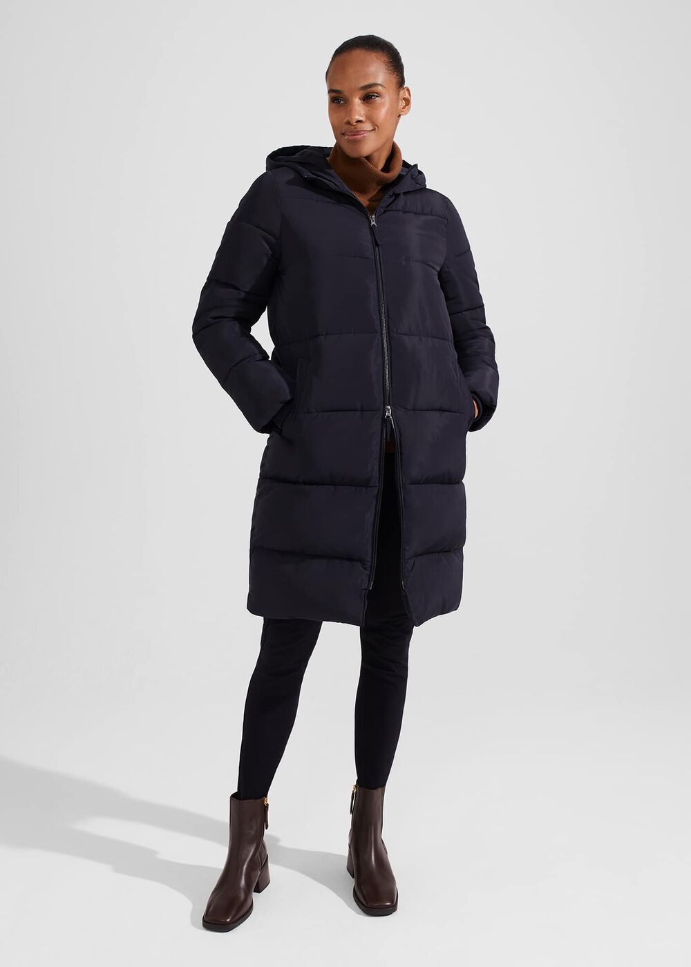 A woman wearing a navy blue puffer coat with a hood, front zipper, and horizontal quilting, standing with her hands in her pockets.