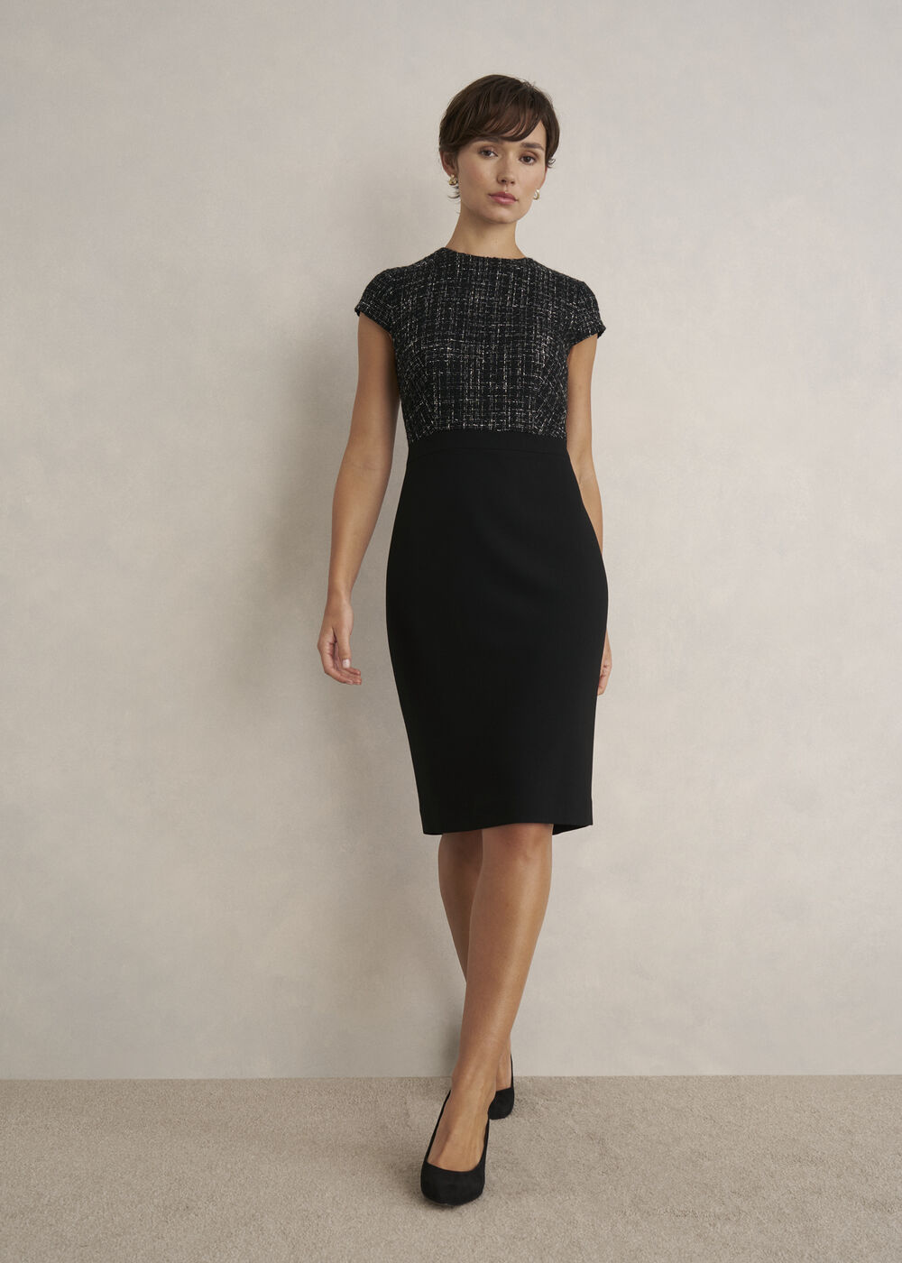 A woman wearing a black dress with a tweed bodice, crew neckline, capped sleeves, and a fitted skirt.