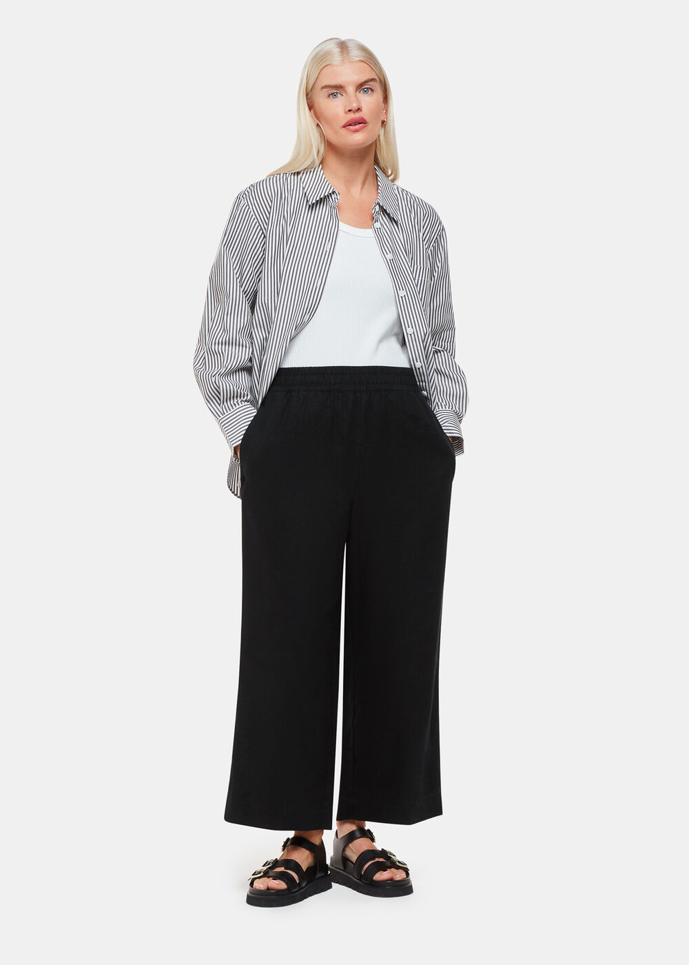 A woman wearing black linen trousers with side pockets, paired with a white top and a striped shirt.