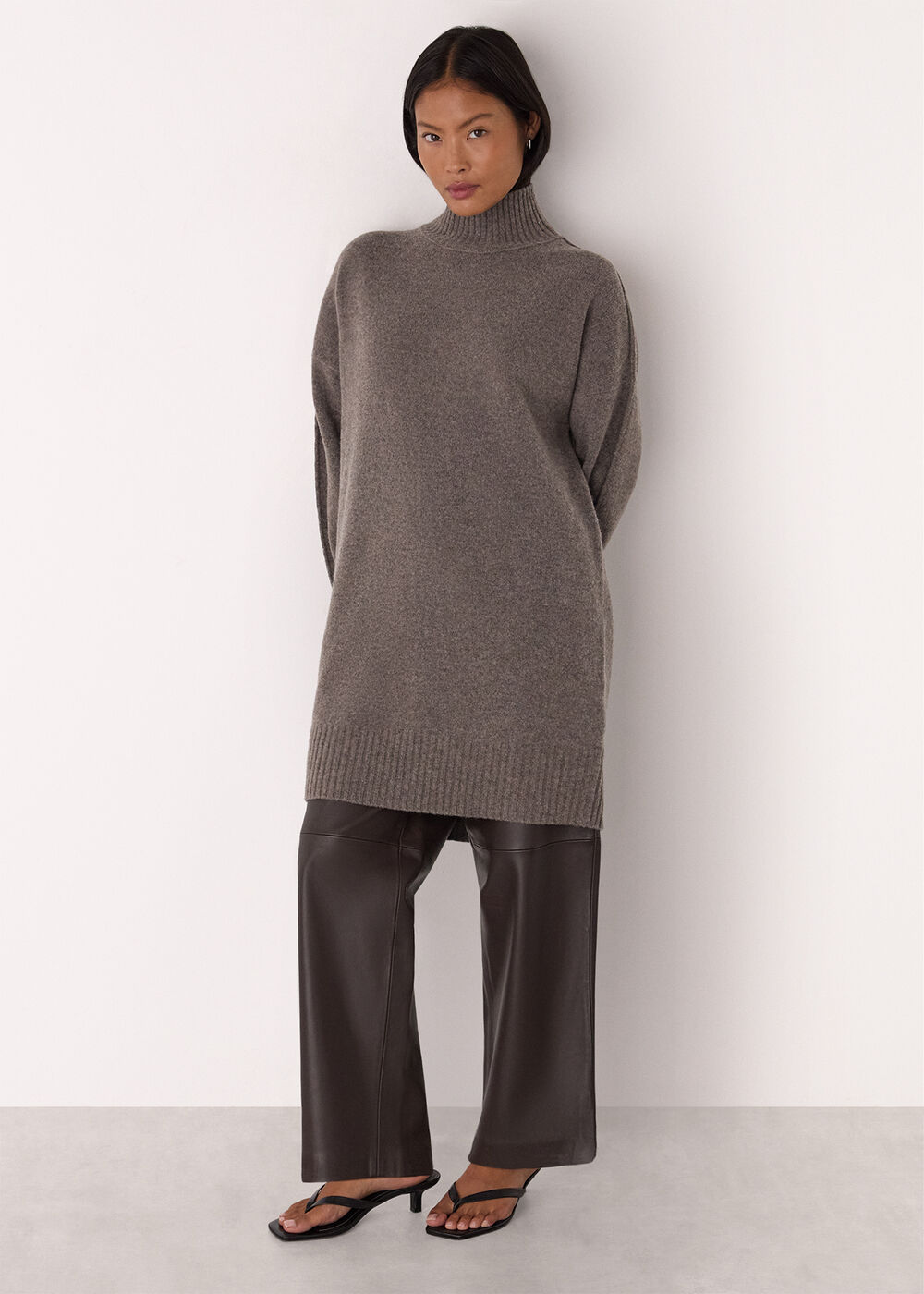 A woman wearing a taupe mini dress with a funnel neck collar, long sleeves, and a relaxed cocoon silhouette.
