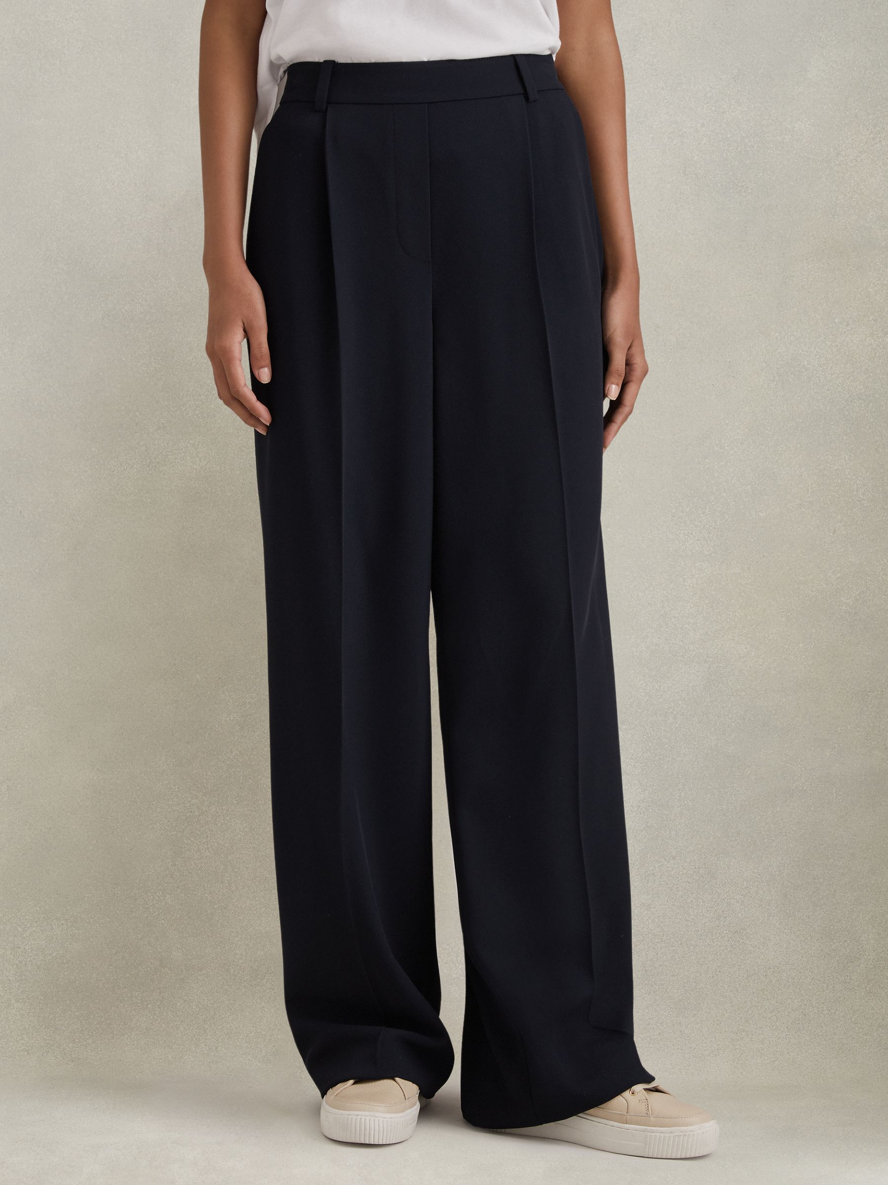 A pair of navy wide-leg trousers with front pleats, a half-elasticated waistband, side pockets, and a woven texture, worn by a person.