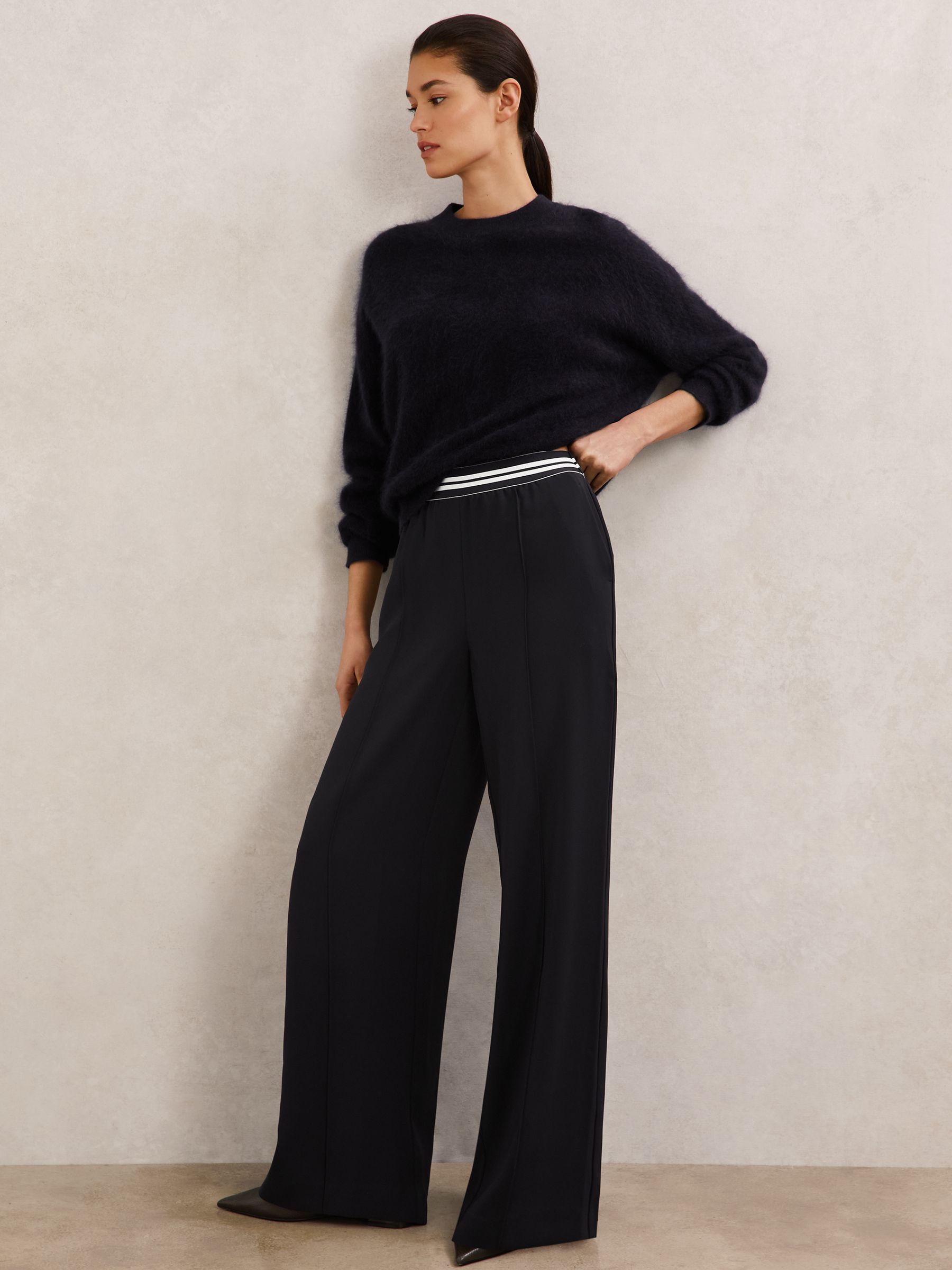 A pair of navy wide-leg trousers with an elasticated striped waistband, front pintucks, and side slip pockets, shown on a female model.