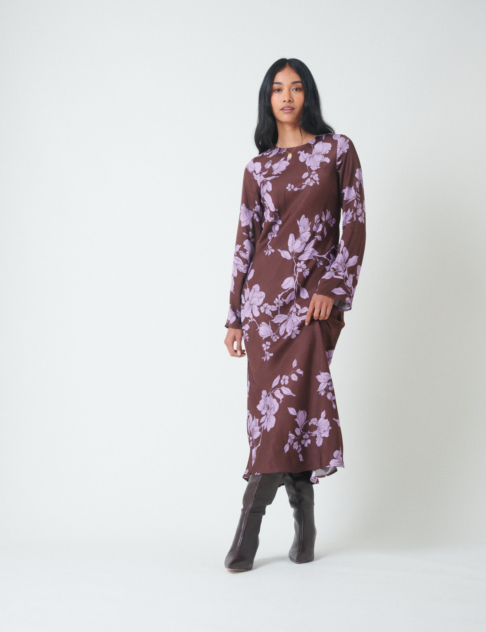 A woman wearing a brown midi dress with purple floral patterns, long fluted sleeves, and a keyhole back fastening.