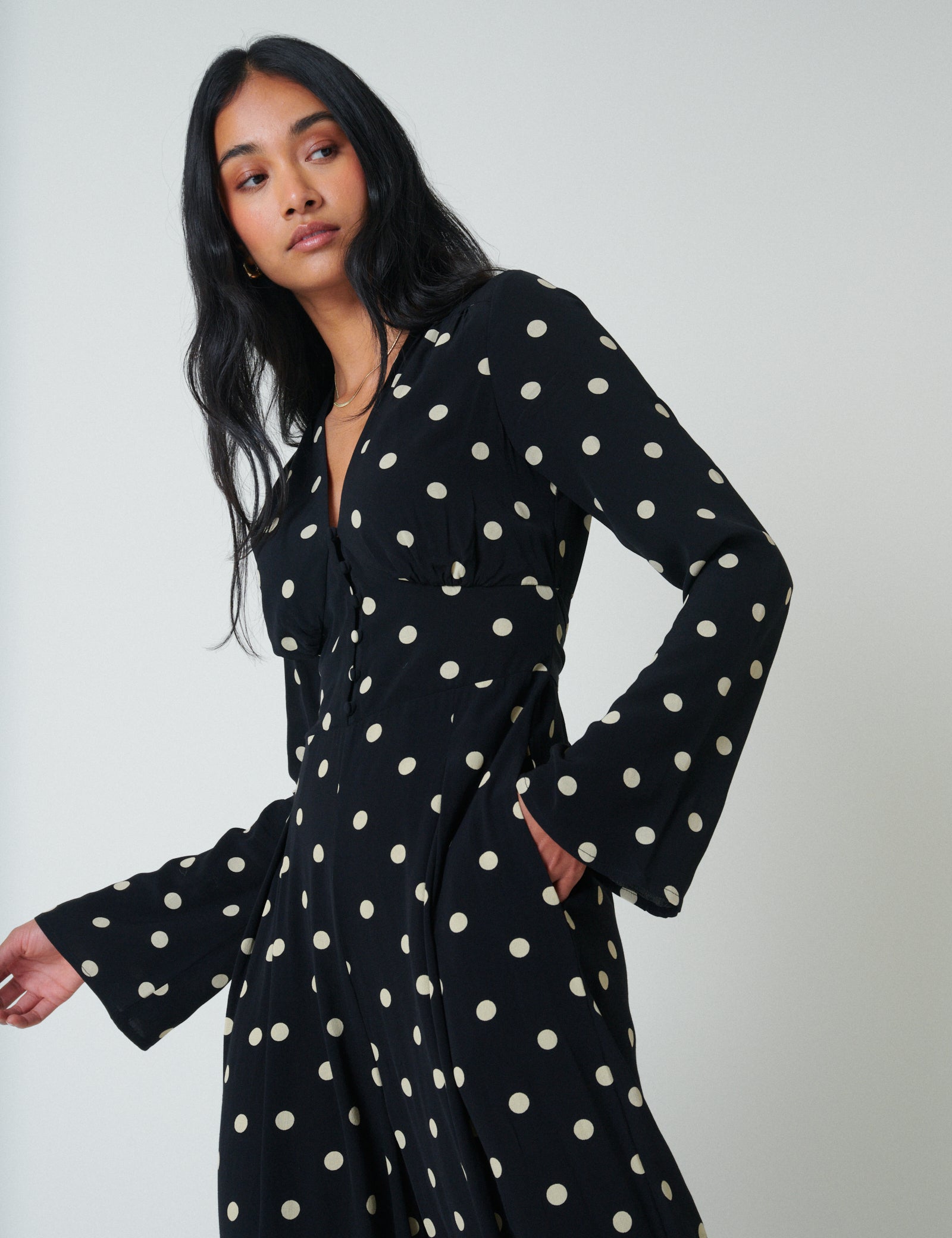 A woman wearing a black polka dot jumpsuit with long sleeves and a V-neckline, standing against a plain background.