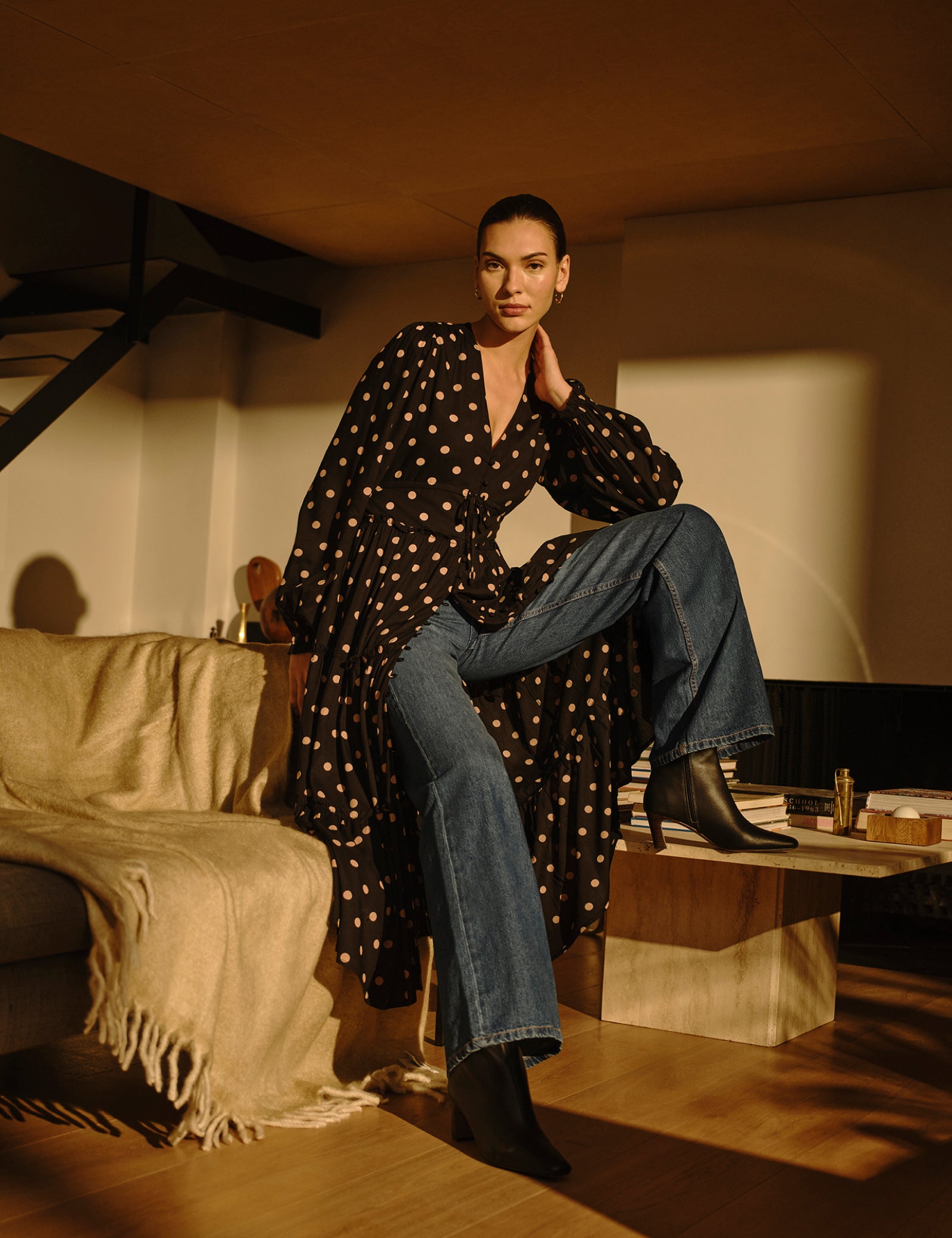 A woman wearing a black midi dress with pink polka dots, long balloon sleeves, a V-neckline, and a tiered skirt, paired with black boots.