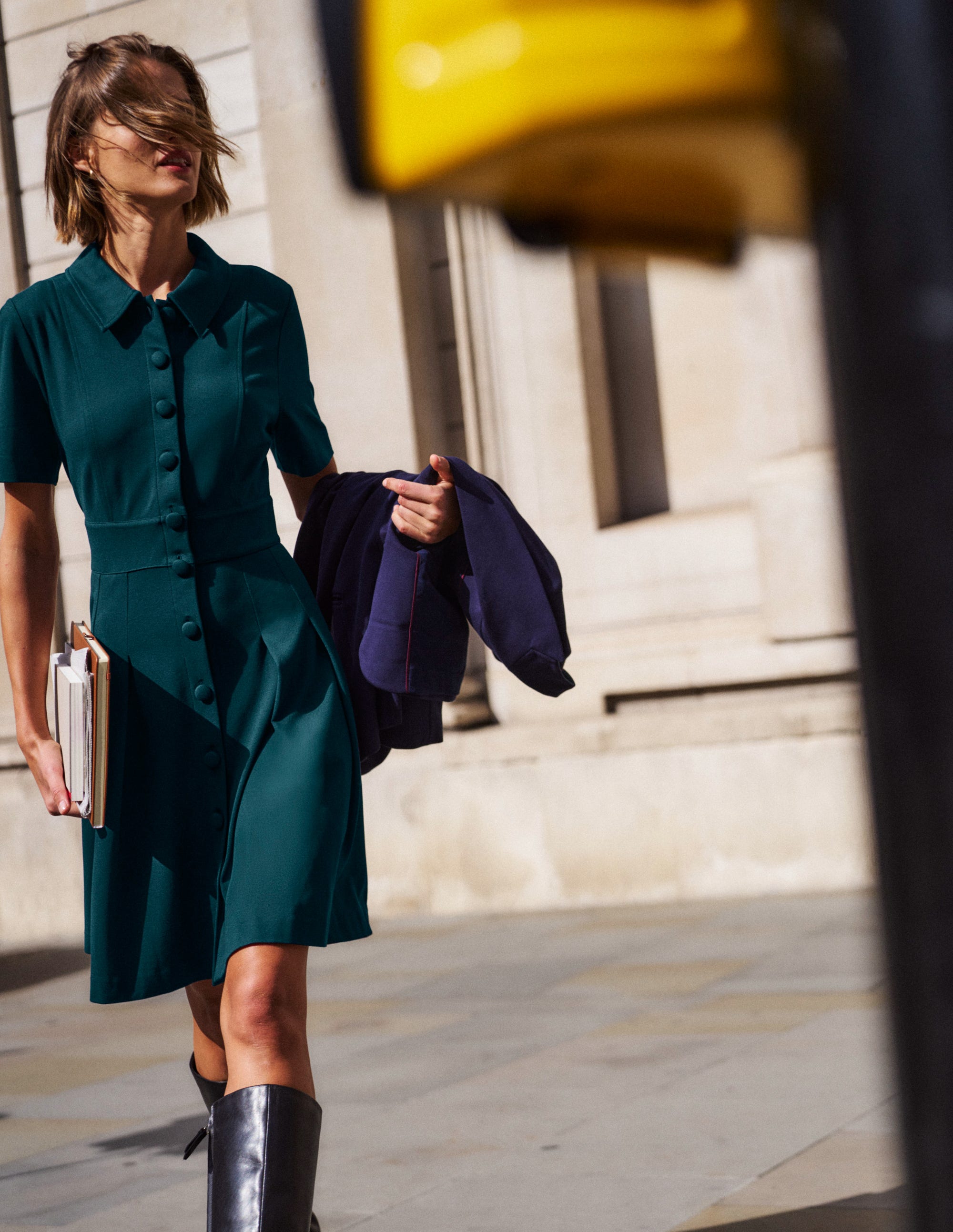 A woman wearing a Midnight Teal ponte short dress with short sleeves, a button-down front, and a fit and flare silhouette, walking outdoors.