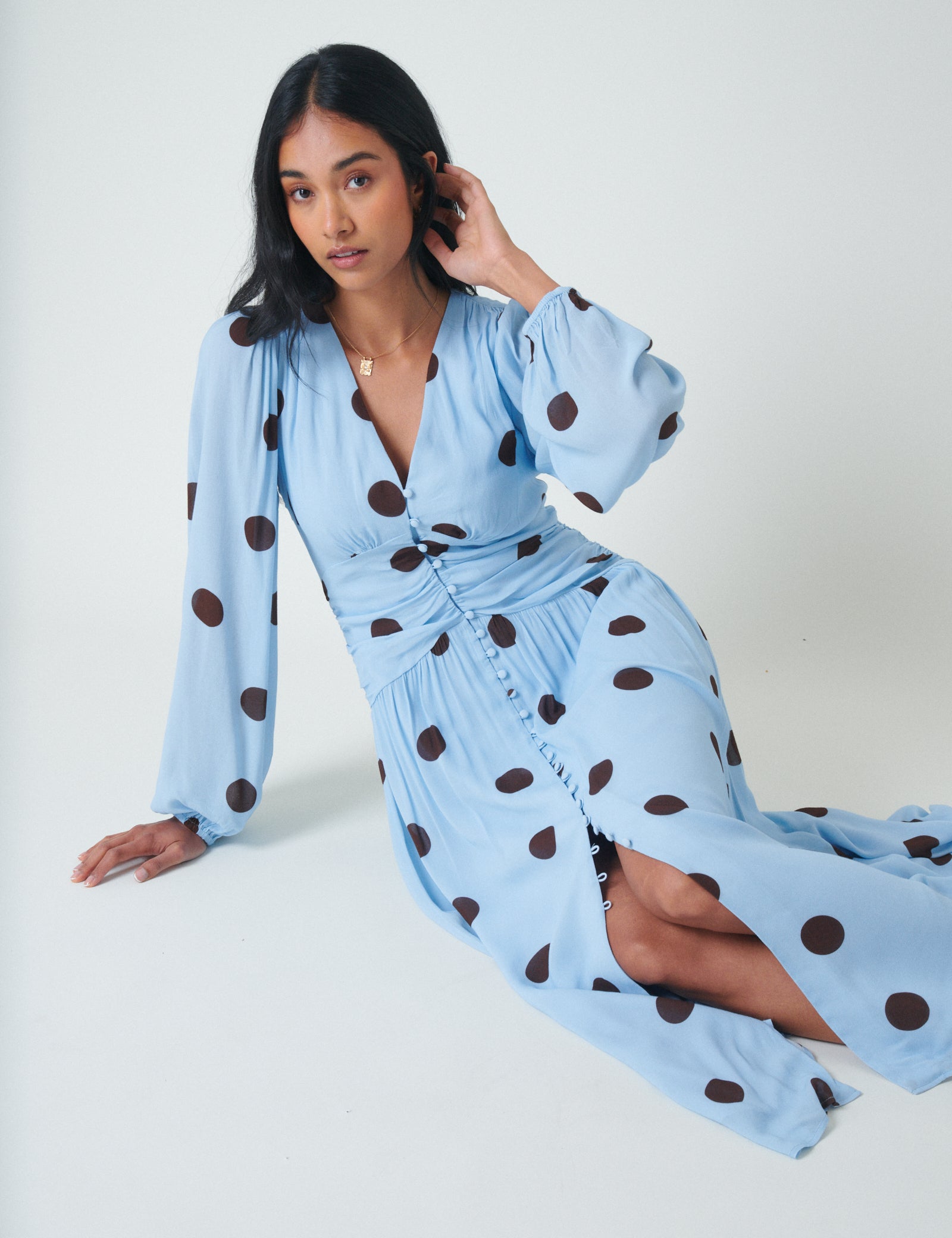 A woman wearing a light blue polka dot midi dress with long sleeves, V-neckline, and front slit.