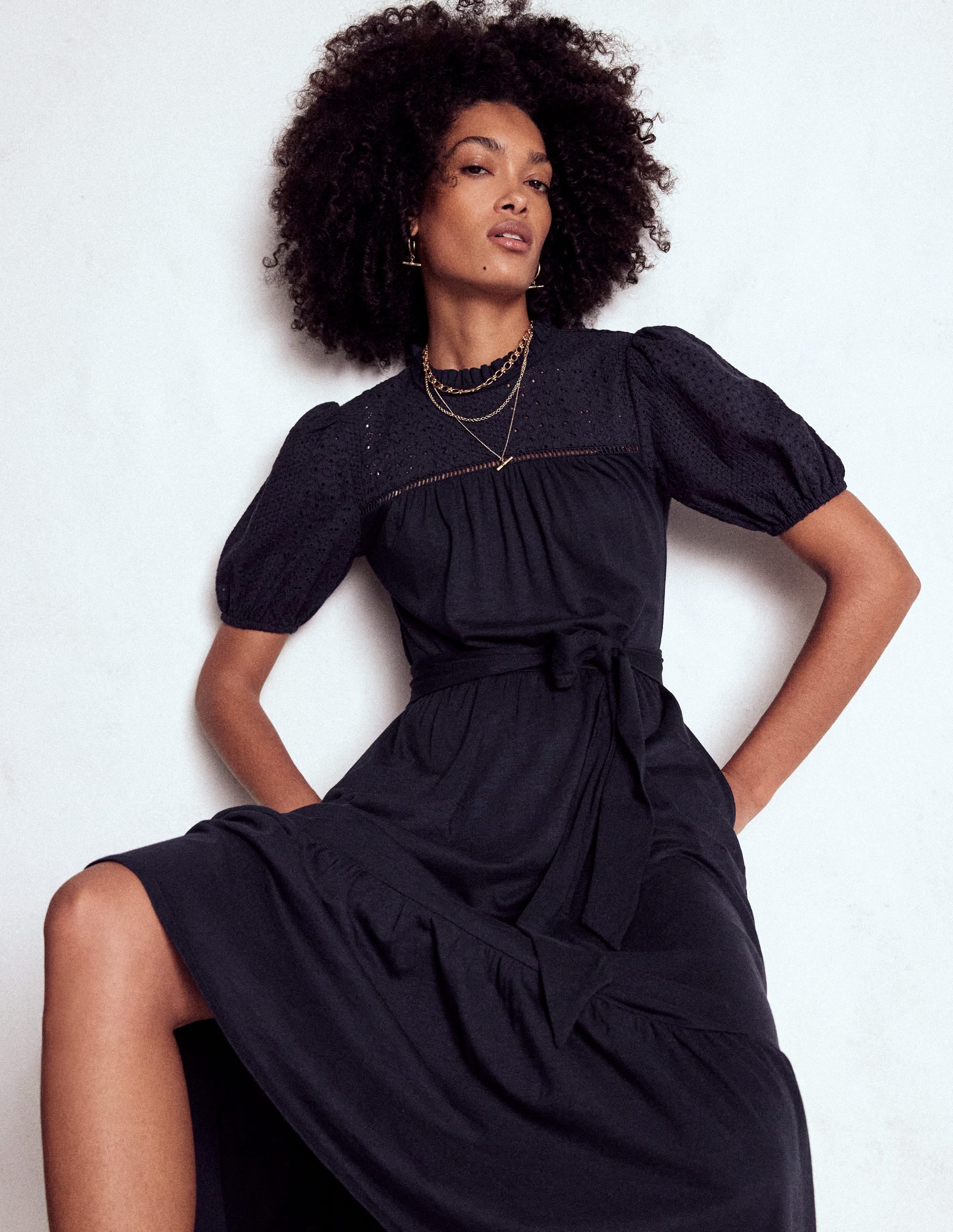 A woman wearing a navy dress with broderie details, billowing sleeves, tiered skirt, and a self-fabric belt.