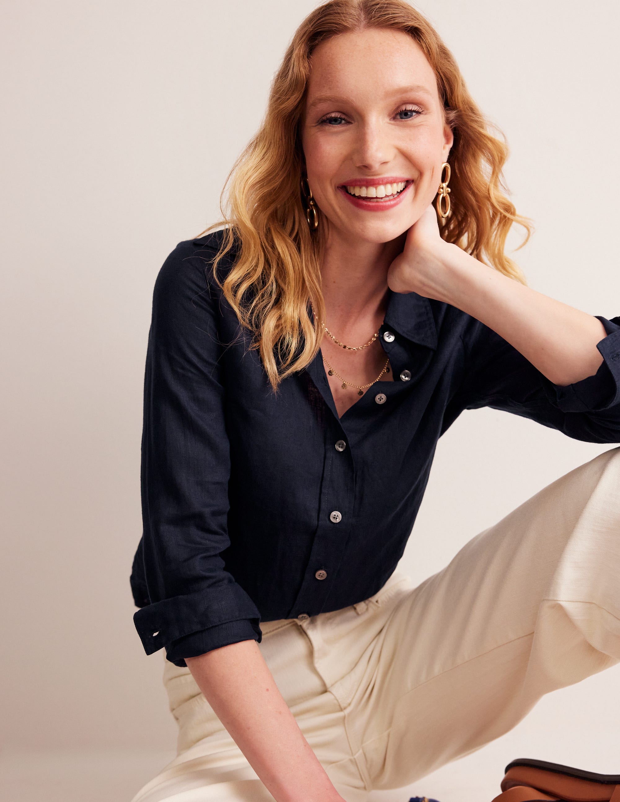 A woman wearing a navy linen shirt with long sleeves and a button-down front, smiling and sitting against a plain background.
