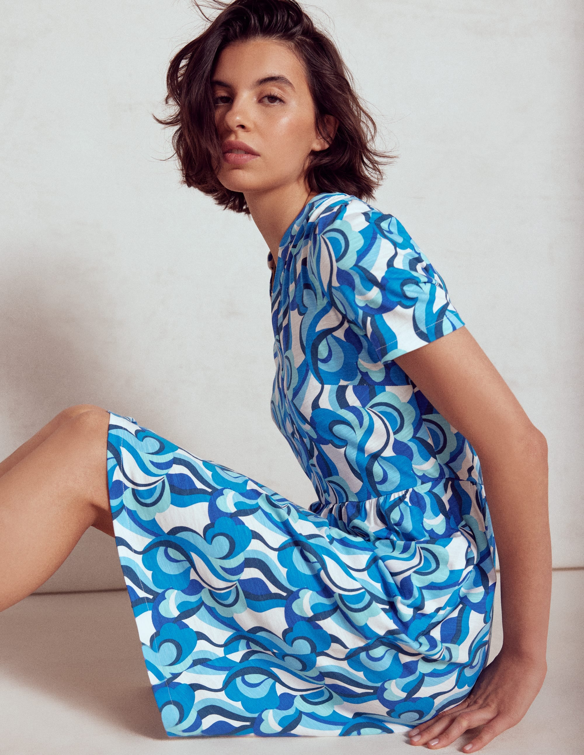 A woman wearing a blue dress with an abstract swirl pattern, short sleeves, and a relaxed fit.