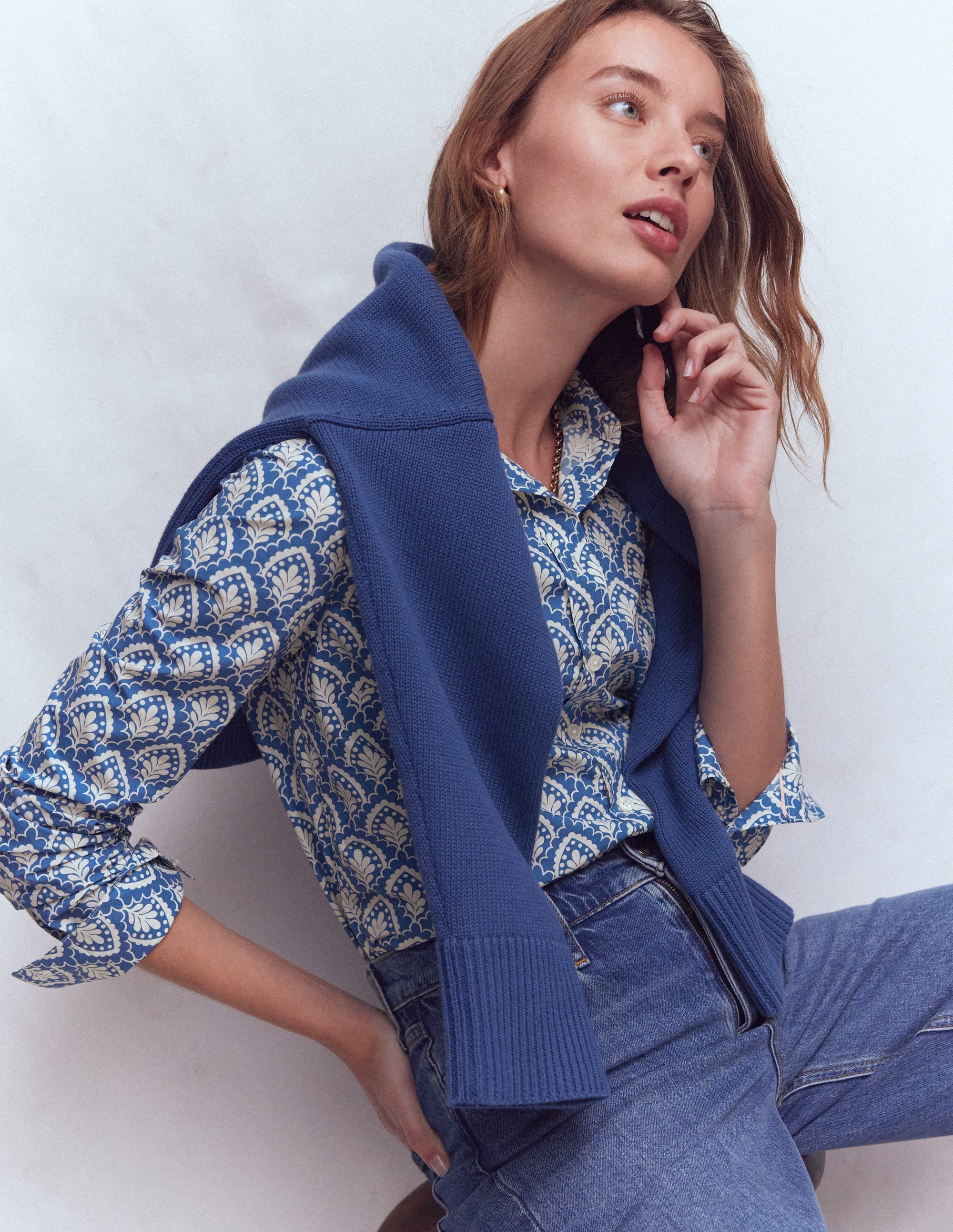 A woman wearing a blue patterned cotton shirt with a curved back hem and a sharp collar, with a blue sweater draped over her shoulders.