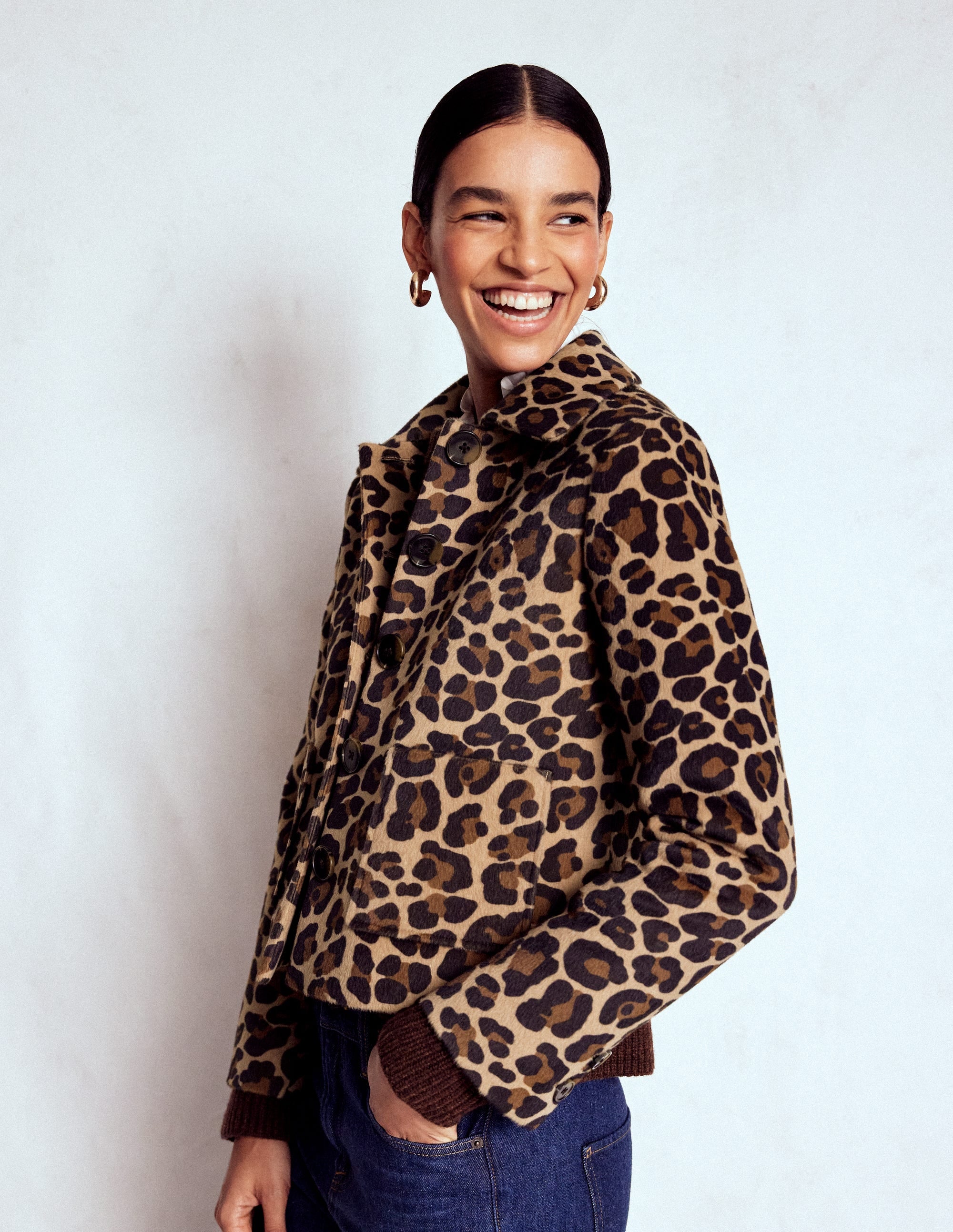 A woman wearing a leopard print jacket with a button front, standing against a plain background, smiling.