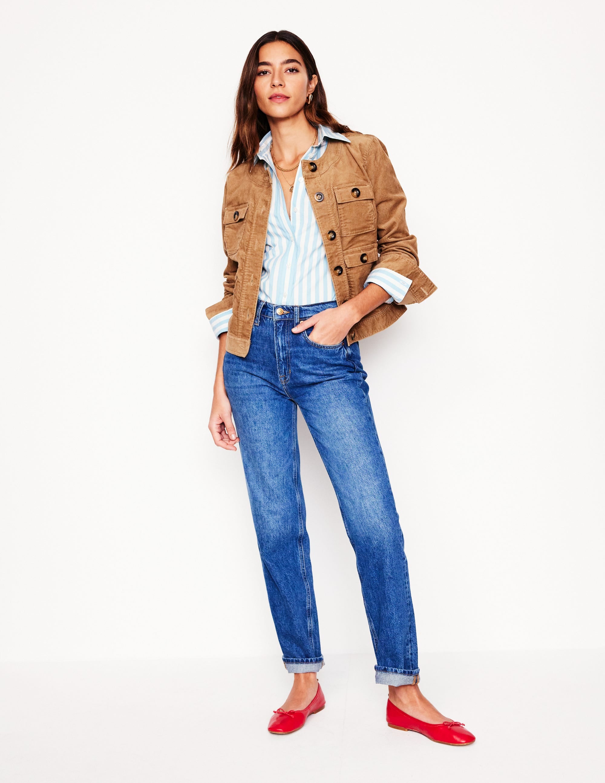 A woman wearing blue high-rise straight-leg jeans with a vintage wash, paired with a striped shirt and a tan jacket.