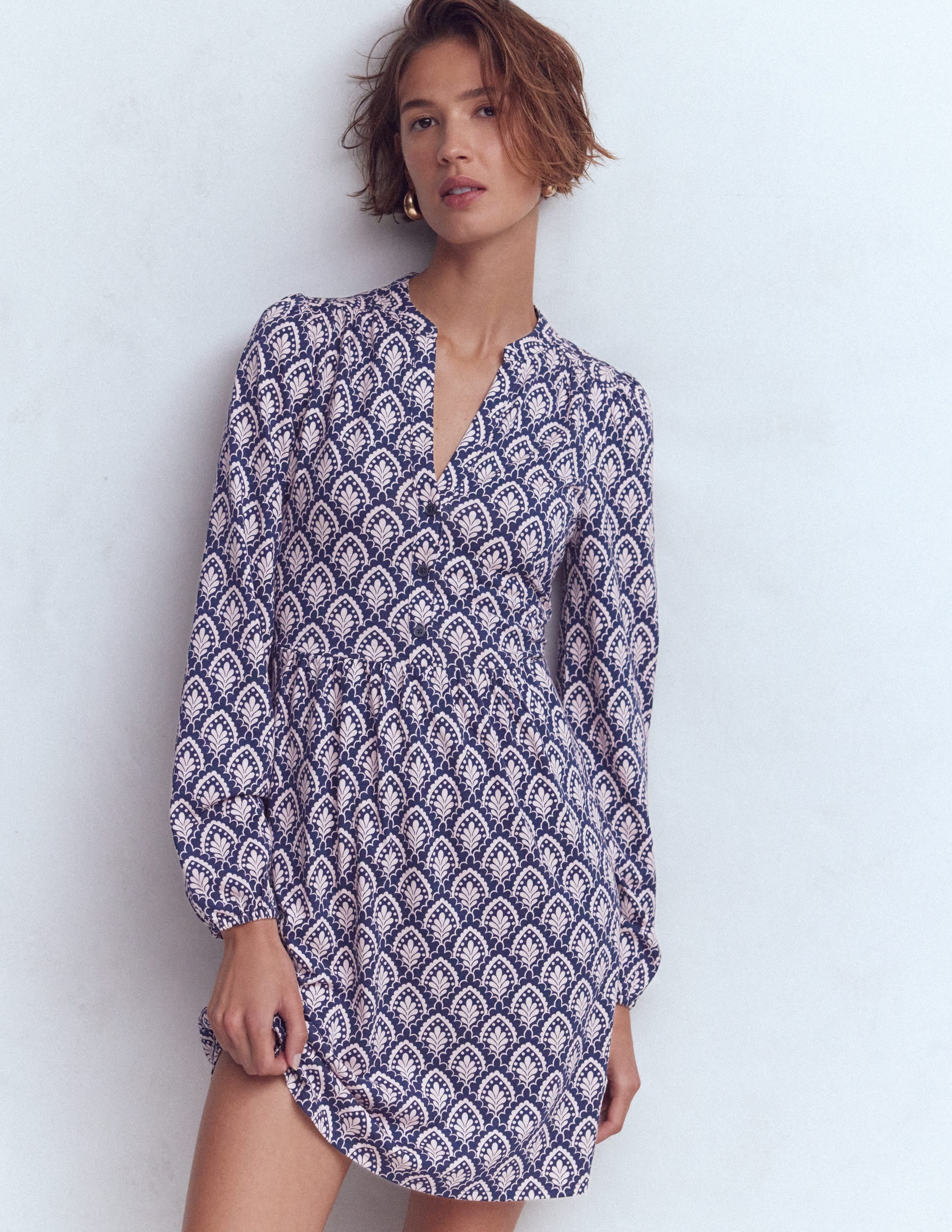 A woman wearing a navy blue and white patterned short jersey dress with blouson sleeves and side pockets.