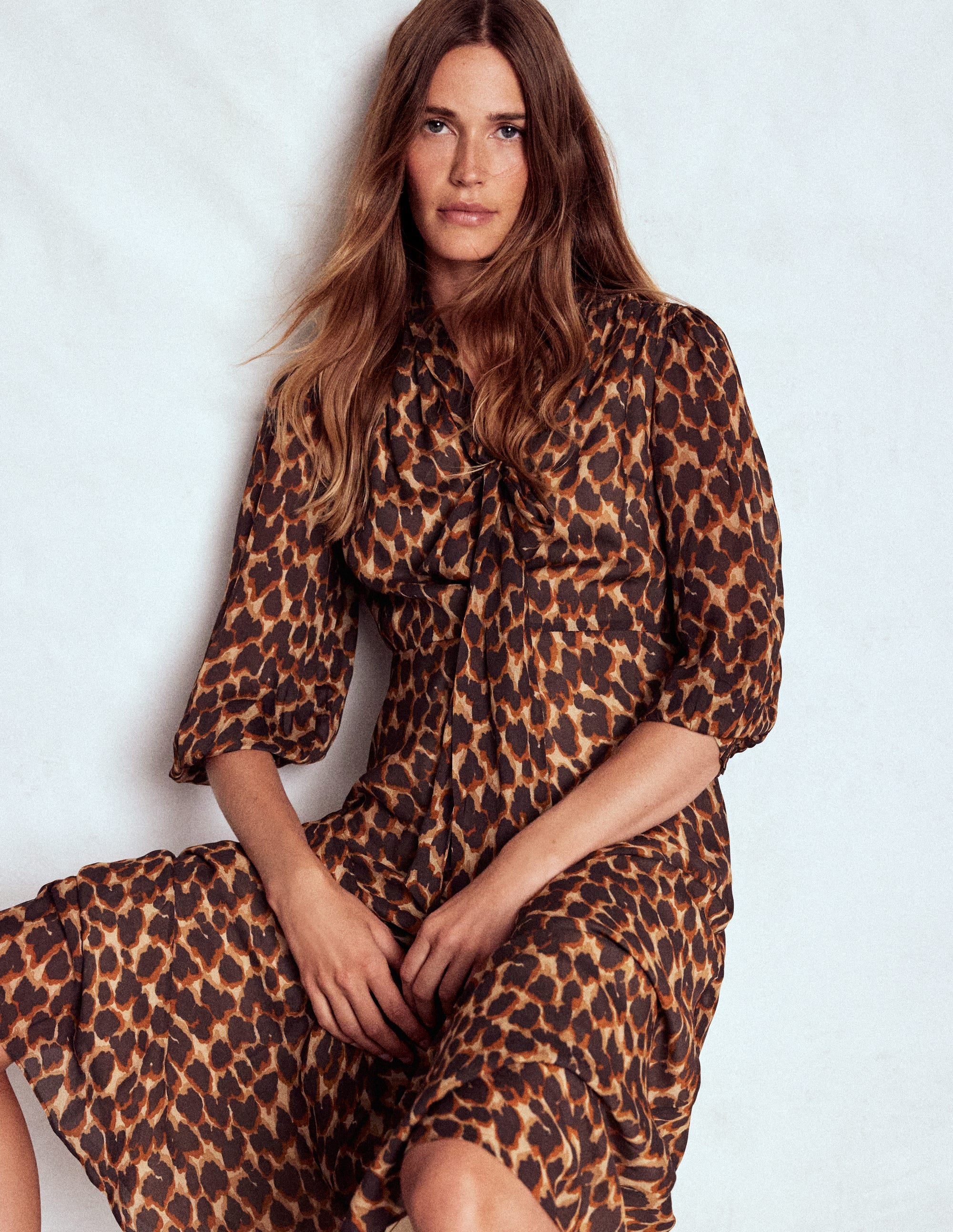 A woman wearing a long dress with a tie neck, puff sleeves, and an abstract leopard print in brown, black, and beige.
