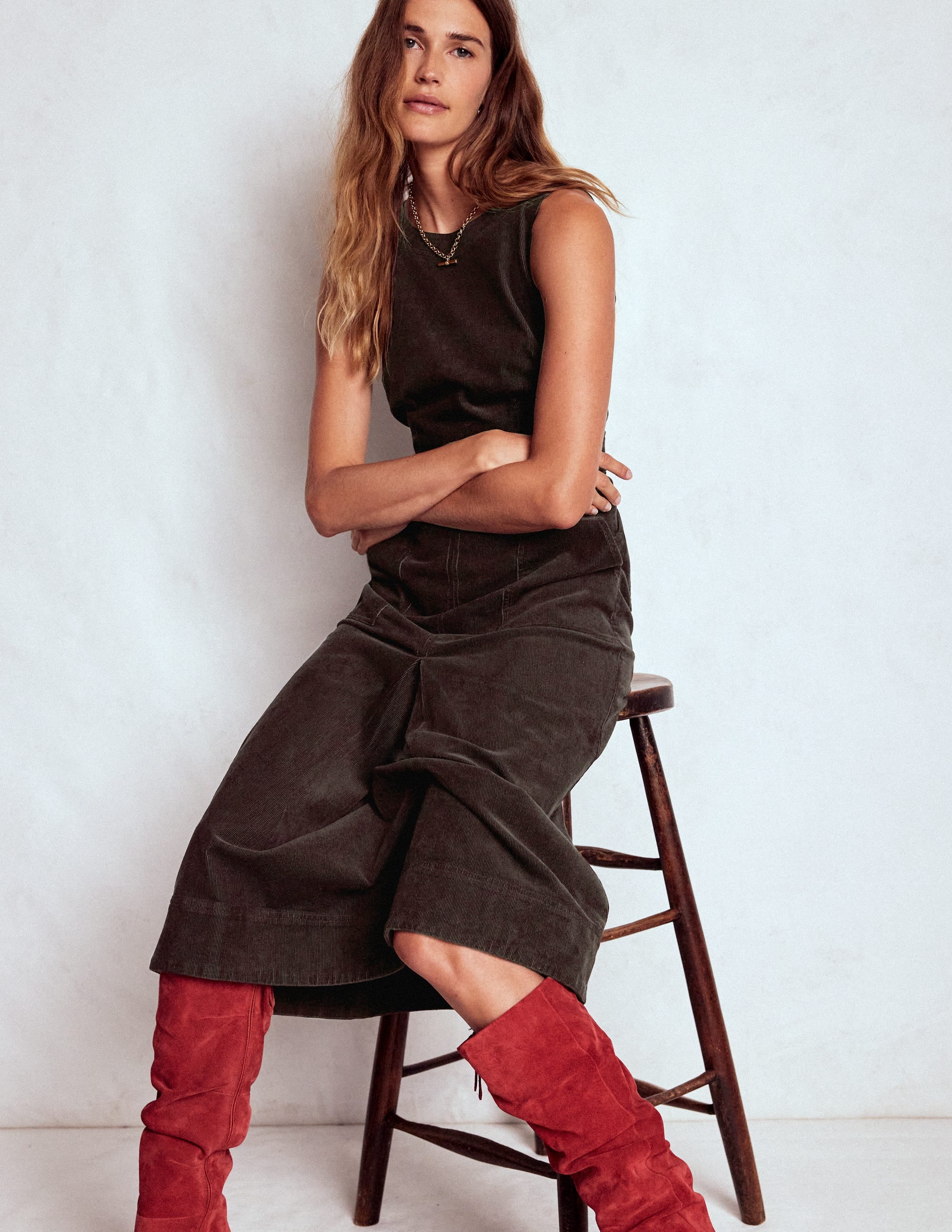 A woman wearing a sleeveless, espresso-colored midi dress with a box pleat design, standing against a plain background.