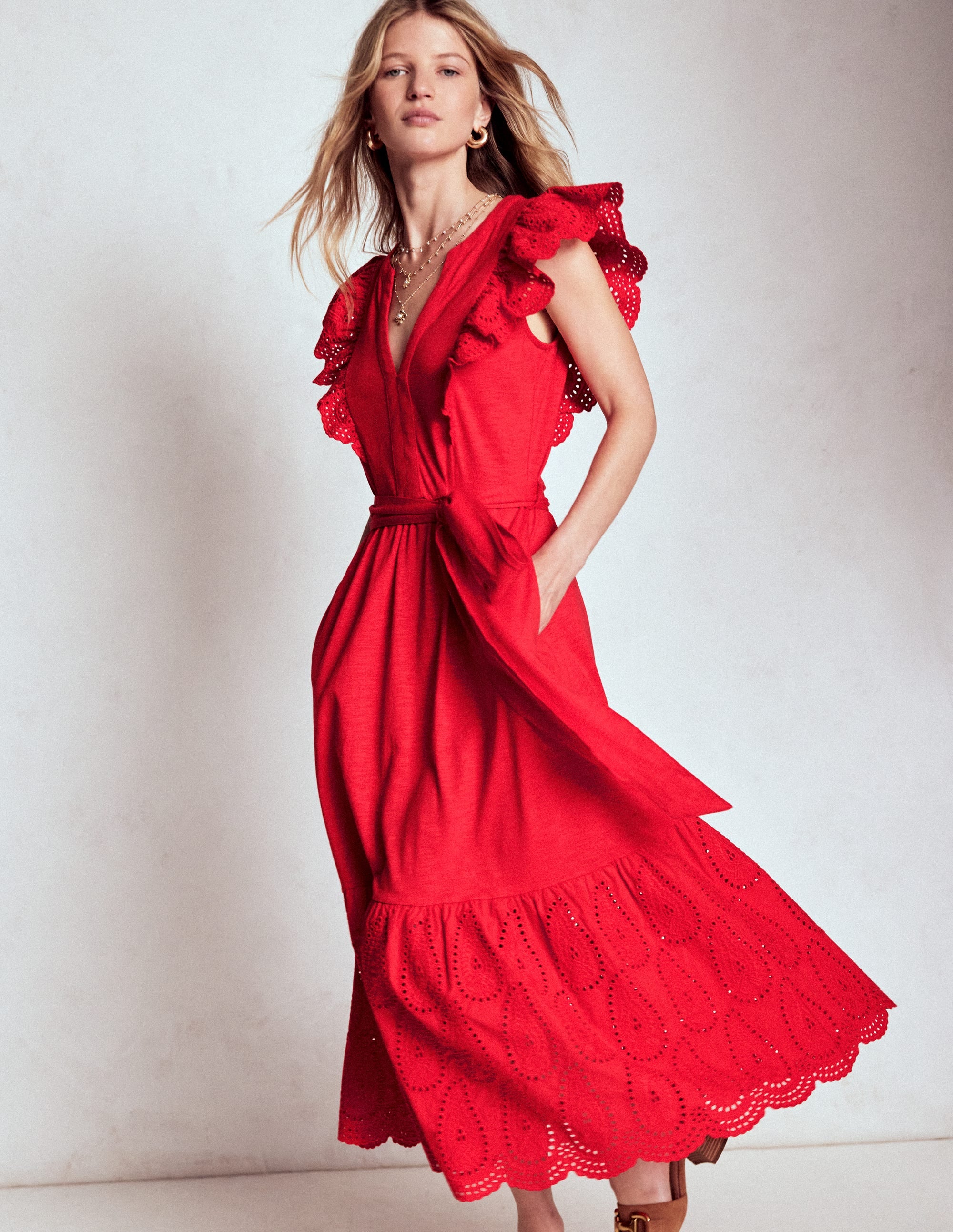 A woman wearing a red ruffle detail tier midi dress with embroidery, fitted waist, and tiered hem, standing against a plain background.