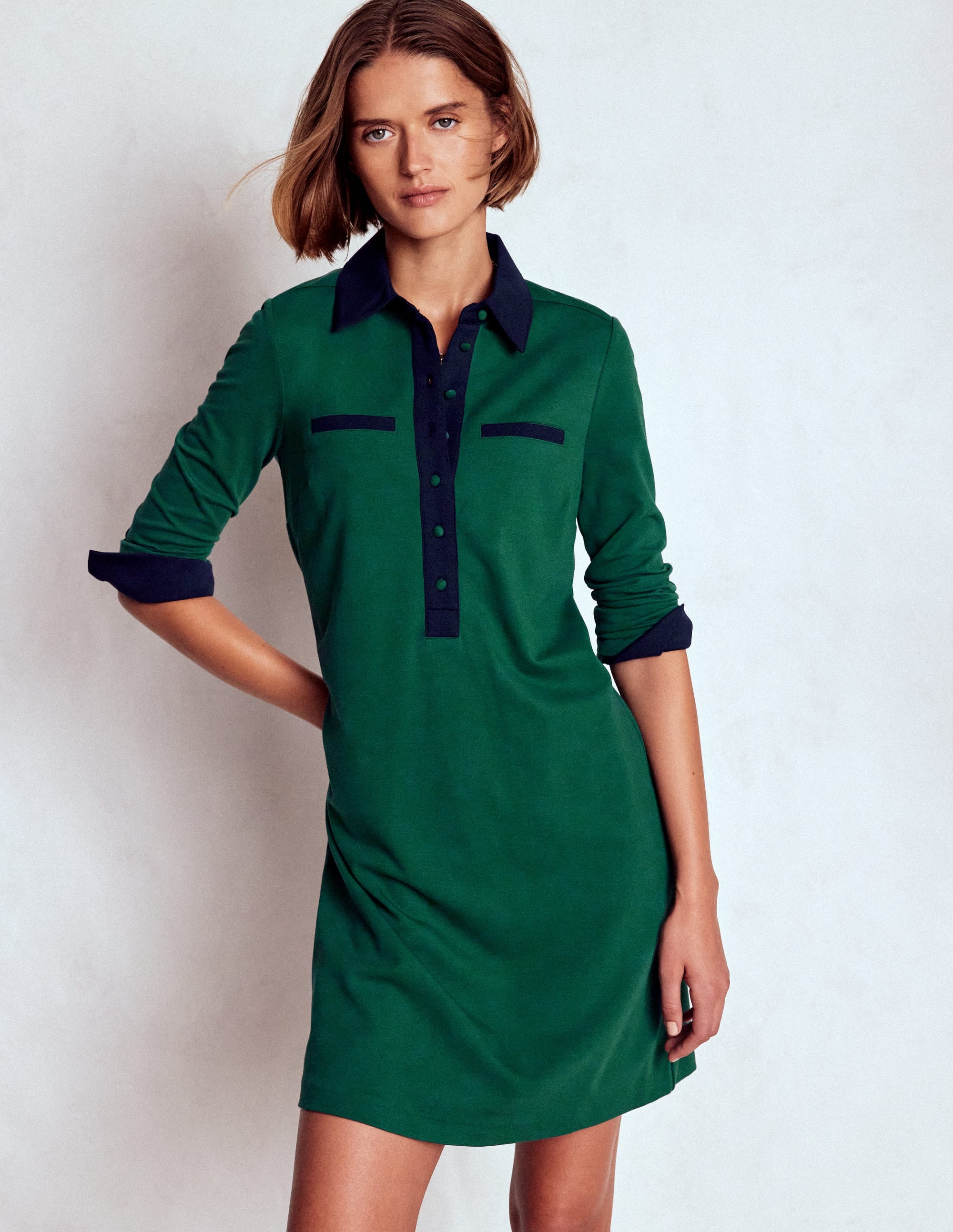 A woman wearing a green ponte dress with navy collar, placket, and pocket details, long sleeves rolled up, and a straight, easy shape.