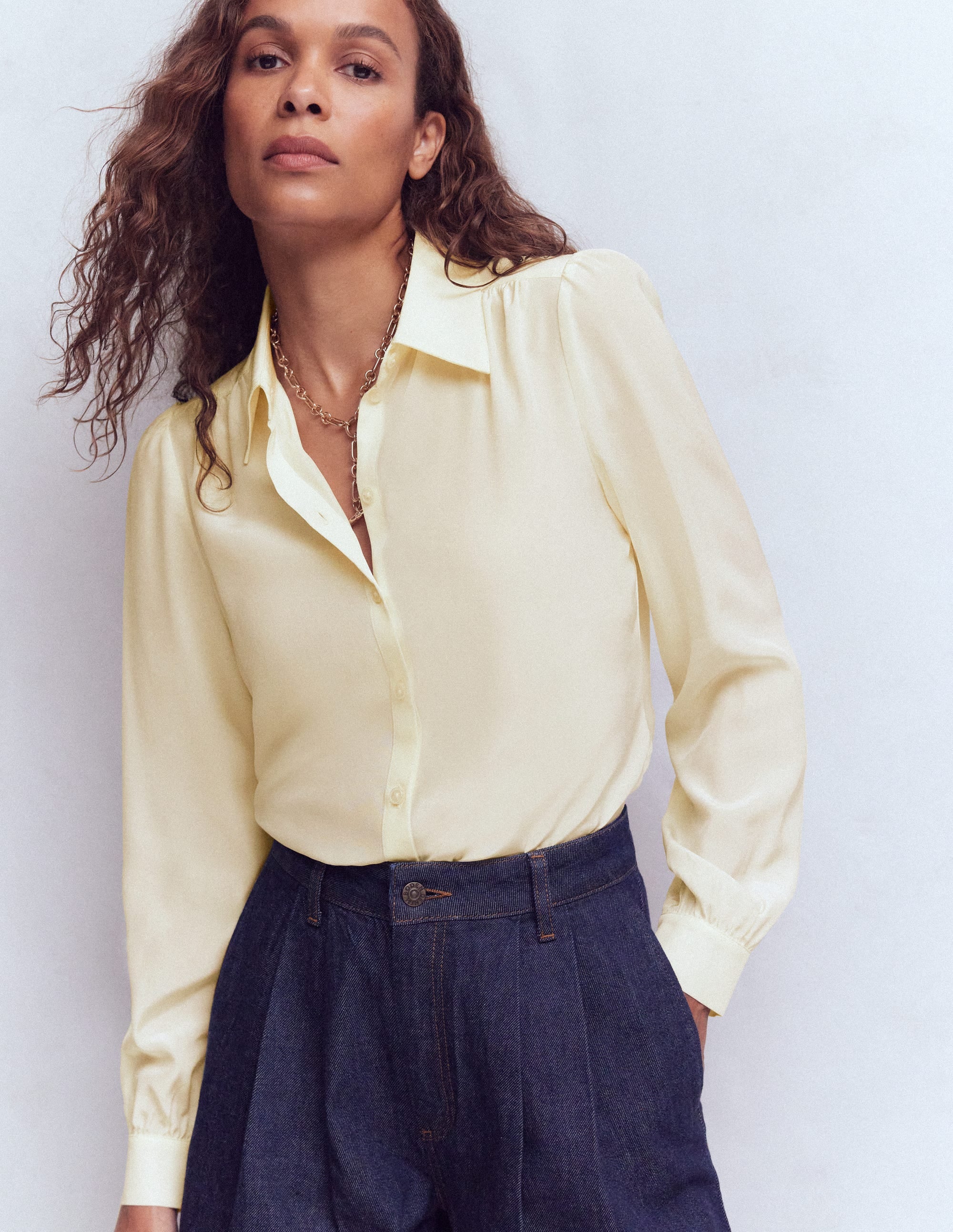 A woman wearing an ivory silk shirt with a classic collar and button-down front, paired with dark high-waisted jeans.