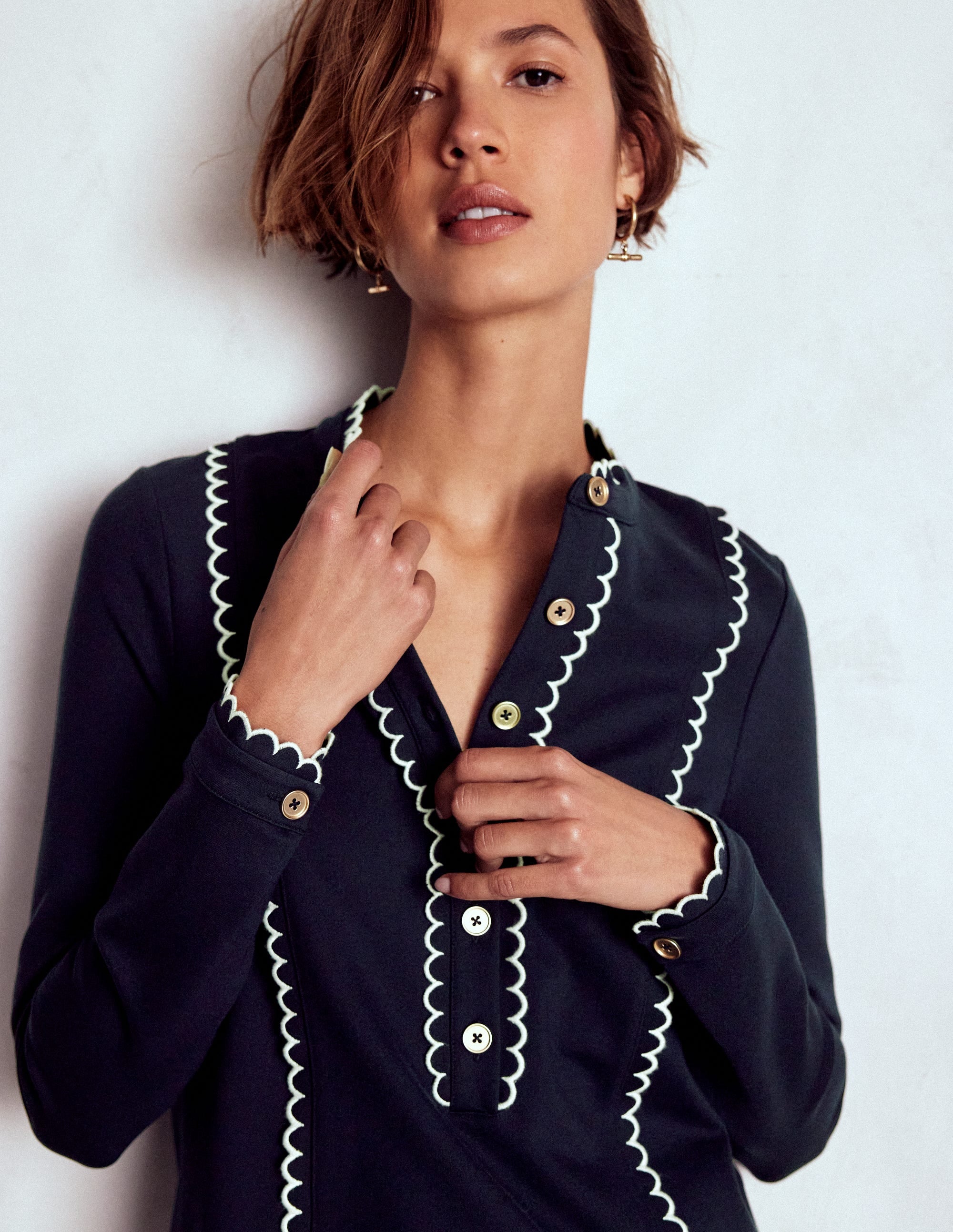 A woman wearing a navy dress with scallop trim on the front and back, shimmering buttons, and a shift silhouette.