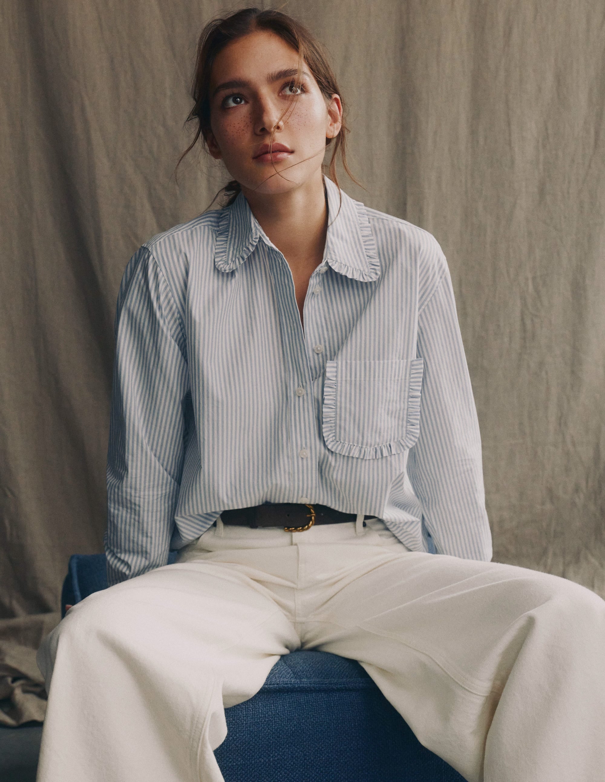 A woman wearing a relaxed-fit cotton shirt with faded denim and ivory stripes, with a collar, button-down front, and a chest pocket.