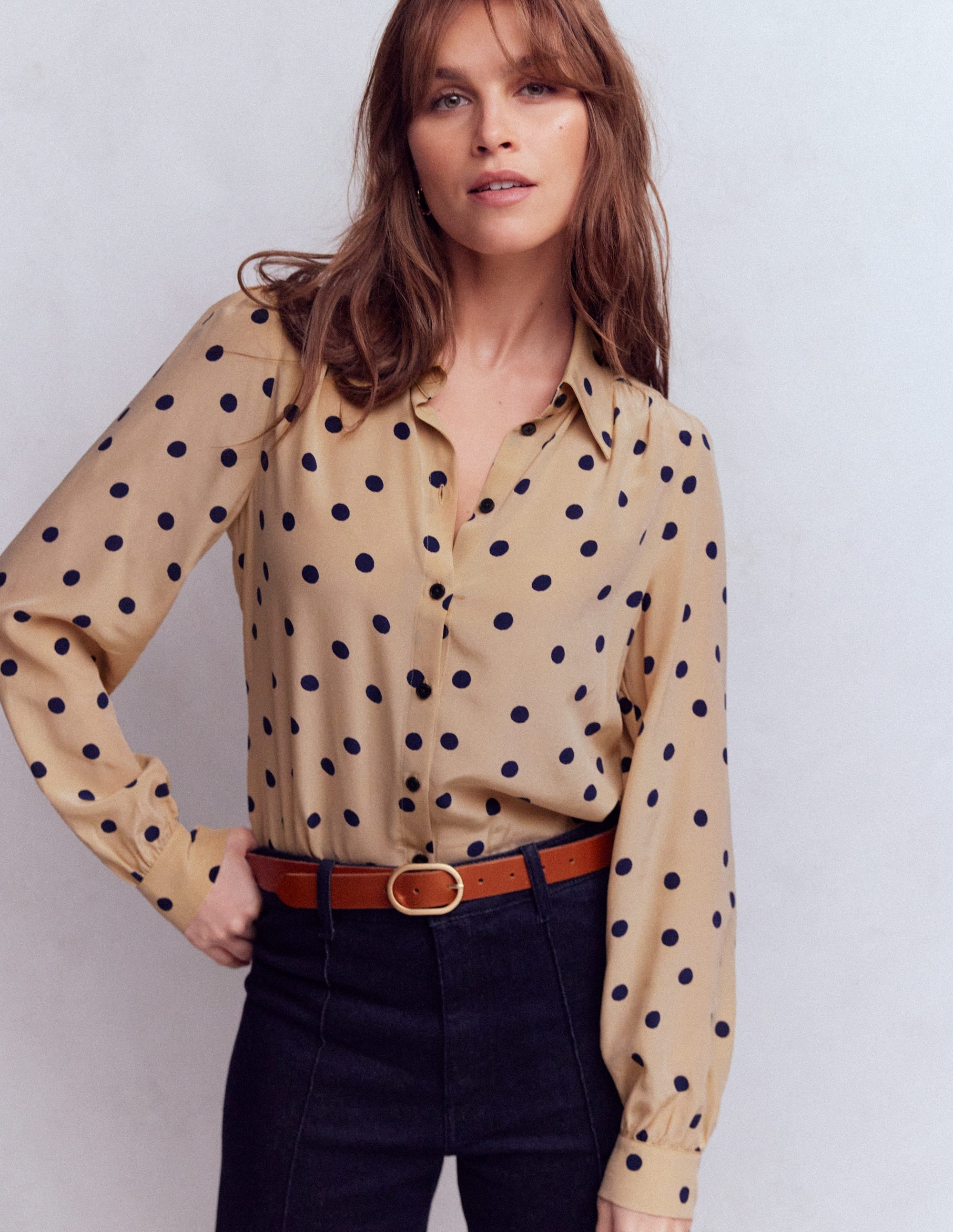 A woman wearing a beige silk shirt with dark navy painted dots, long sleeves, and a classic collar.