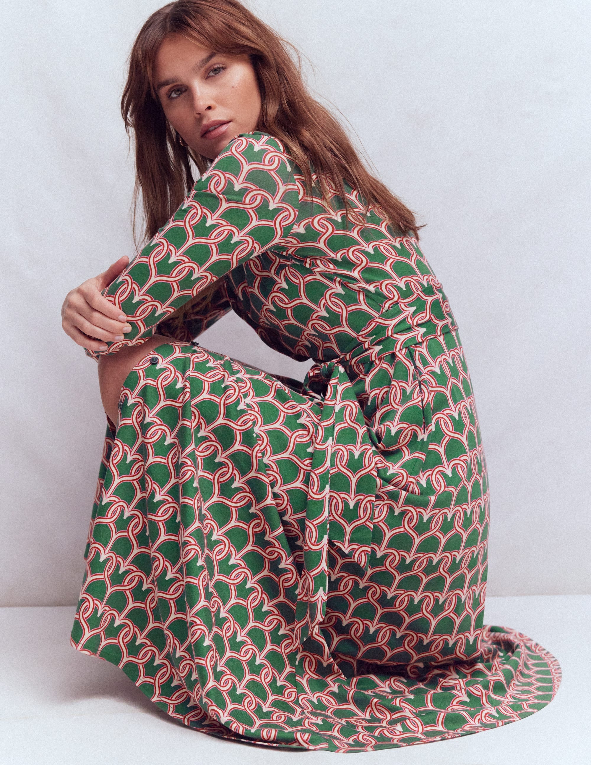 A woman wearing a hunter green jersey shirt dress with a red and white heart link pattern, long sleeves, and a self-fabric belt.