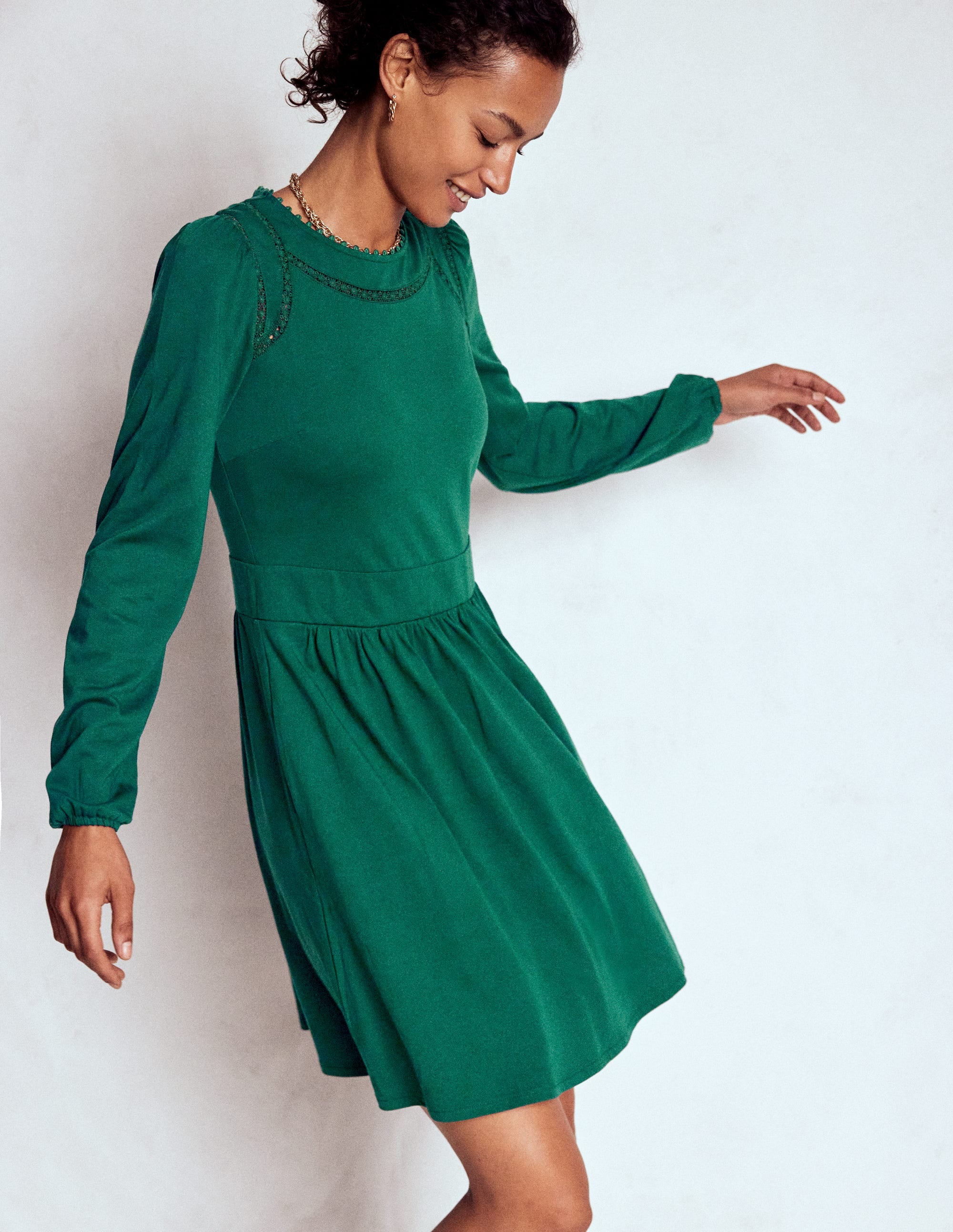 A woman wearing a green short jersey dress with a fit and flare silhouette, long sleeves, and a flippy skirt.