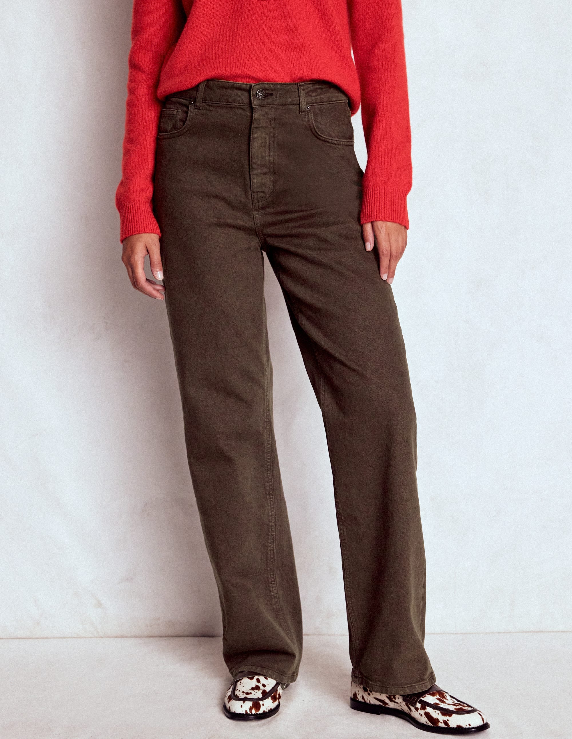 A woman wearing chocolate brown high-rise jeans with a straight leg cut, paired with a red sweater and cow-print shoes.