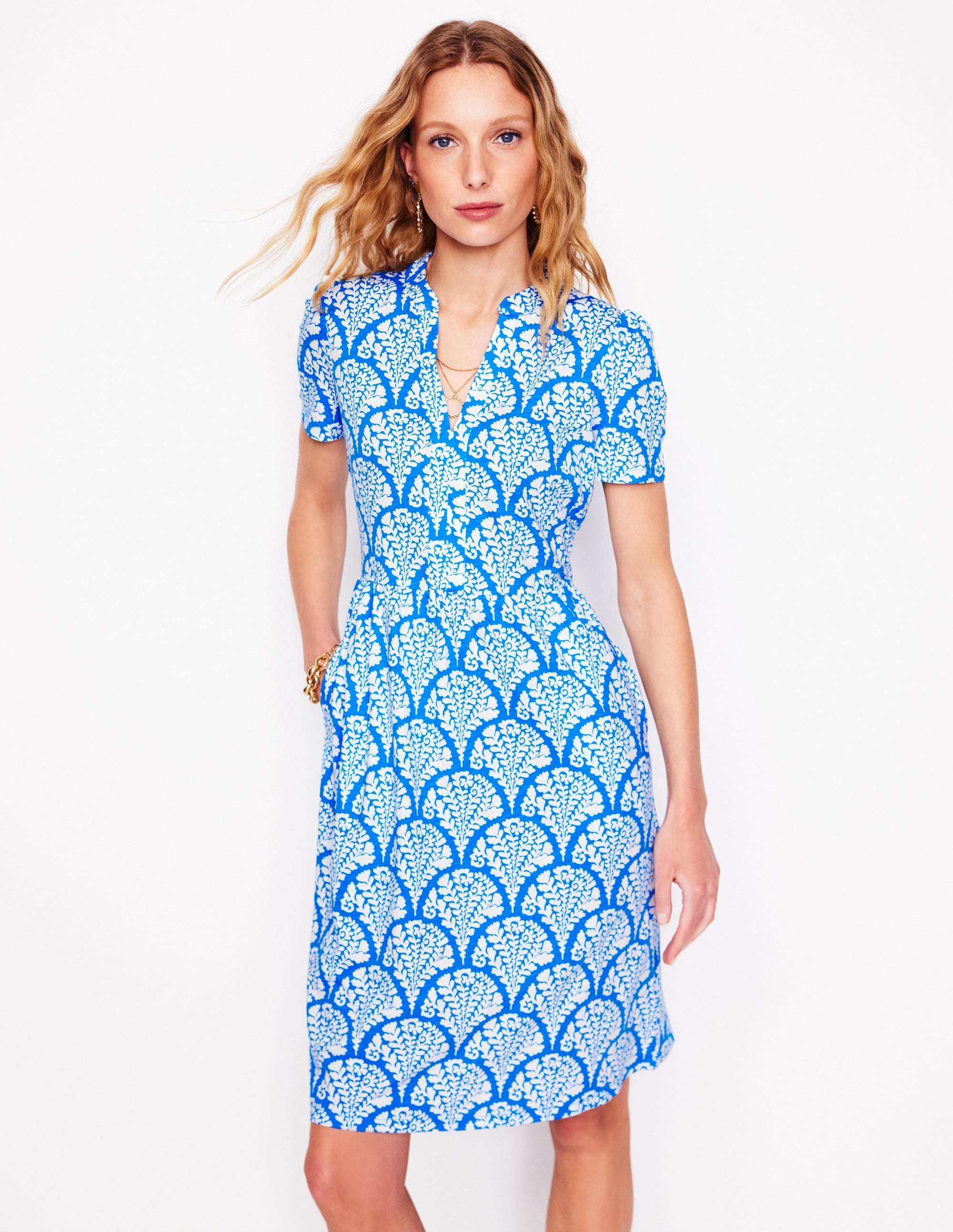 A woman wearing a cerulean blue short jersey dress with a blossomy pattern, short sleeves, and a V-neckline.