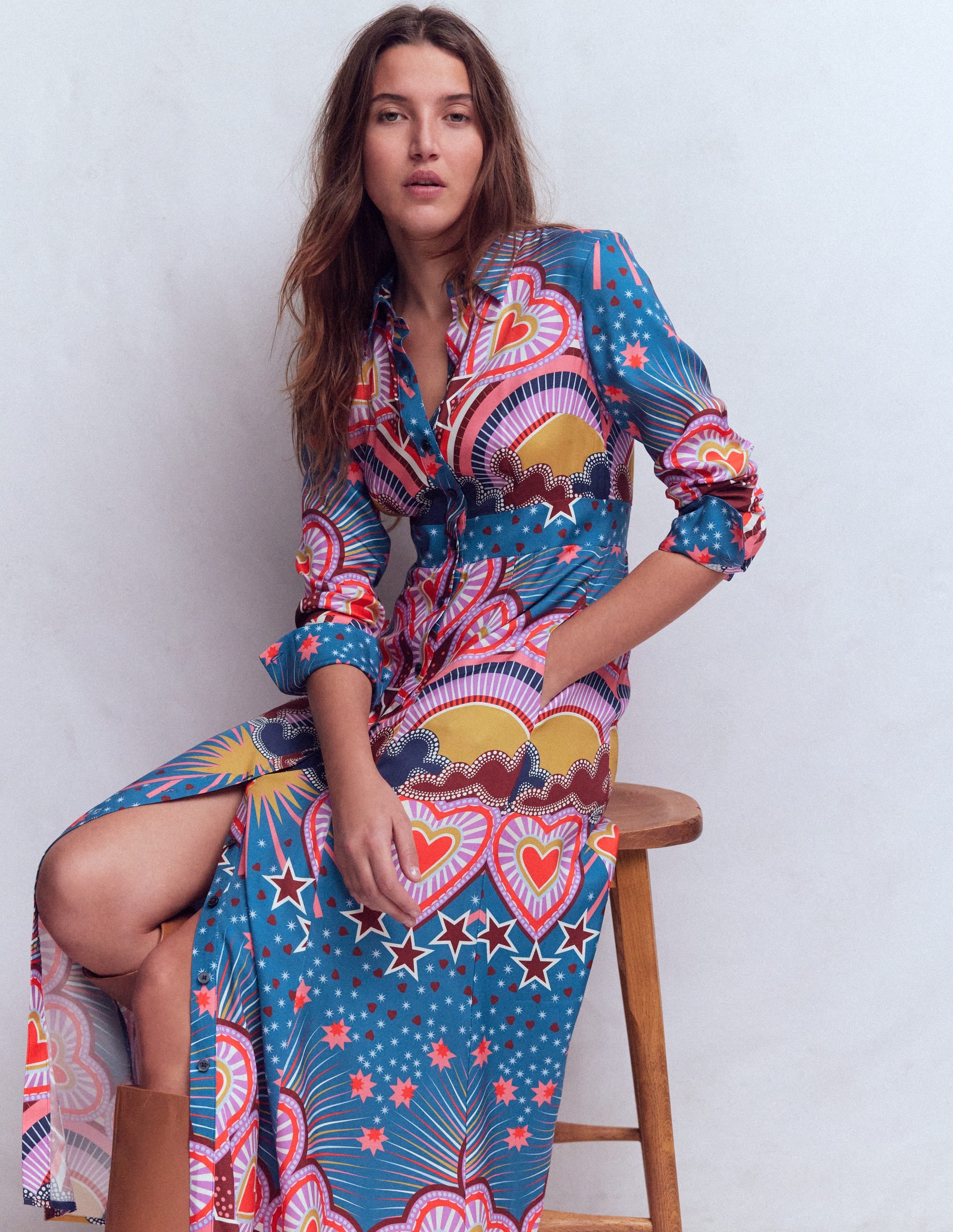 A woman wearing a long, colorful shirt dress with a heart print, standing against a plain background.