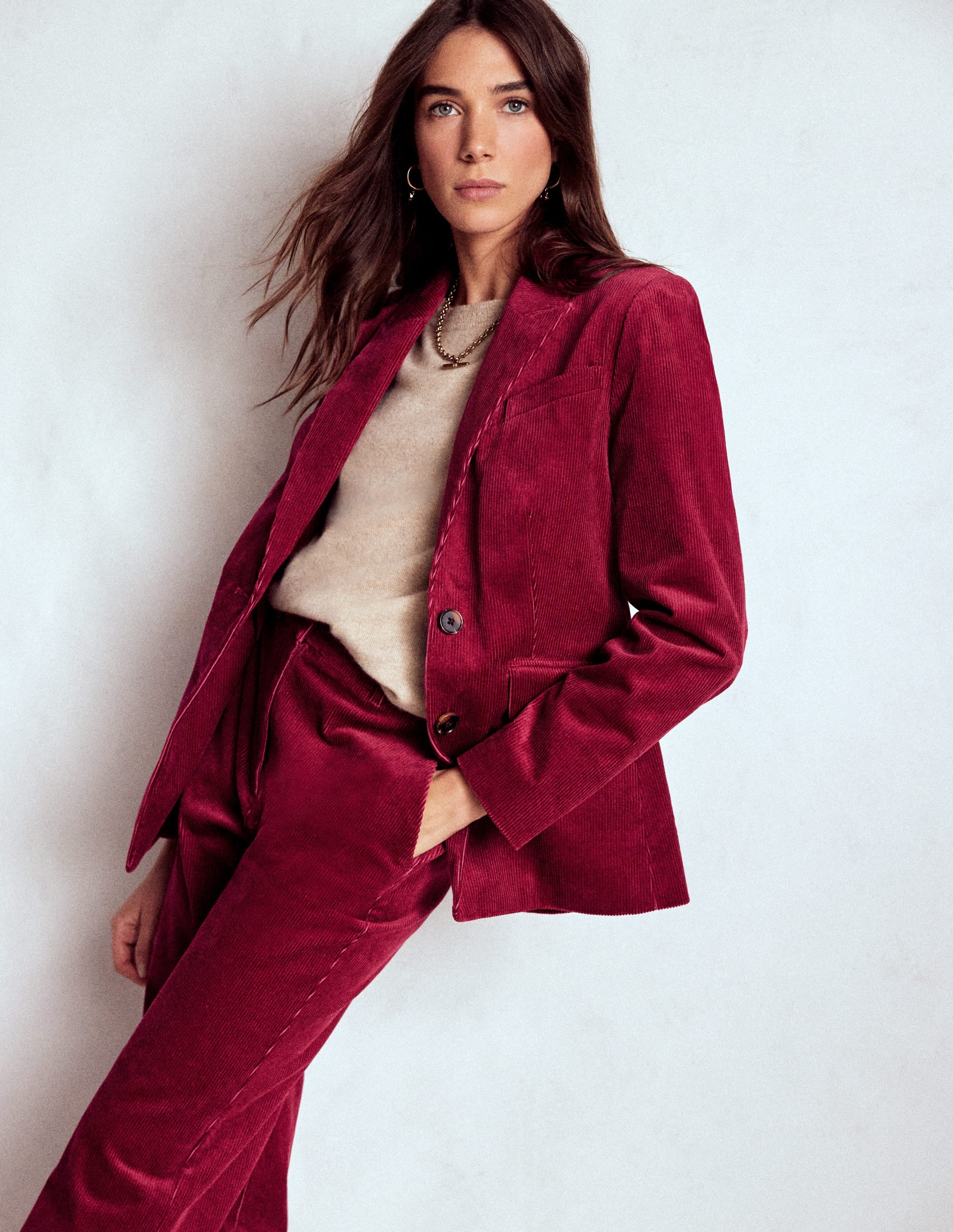 A woman wearing a burgundy red cord blazer with a fitted silhouette, classic lapel, and functional pockets, paired with matching cord trousers.