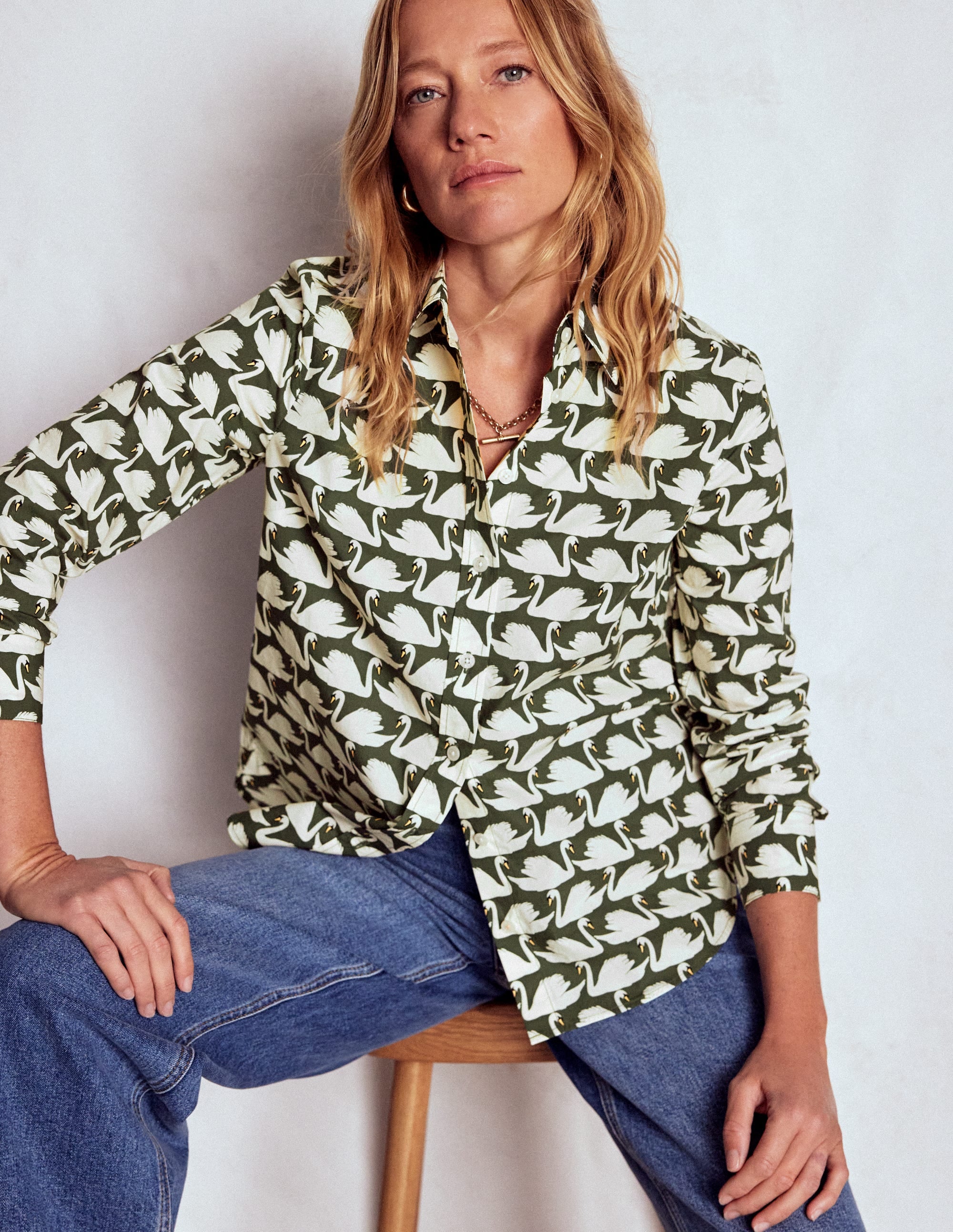 A woman wearing a green cotton shirt with a white swan pattern, long sleeves, and a classic collar.