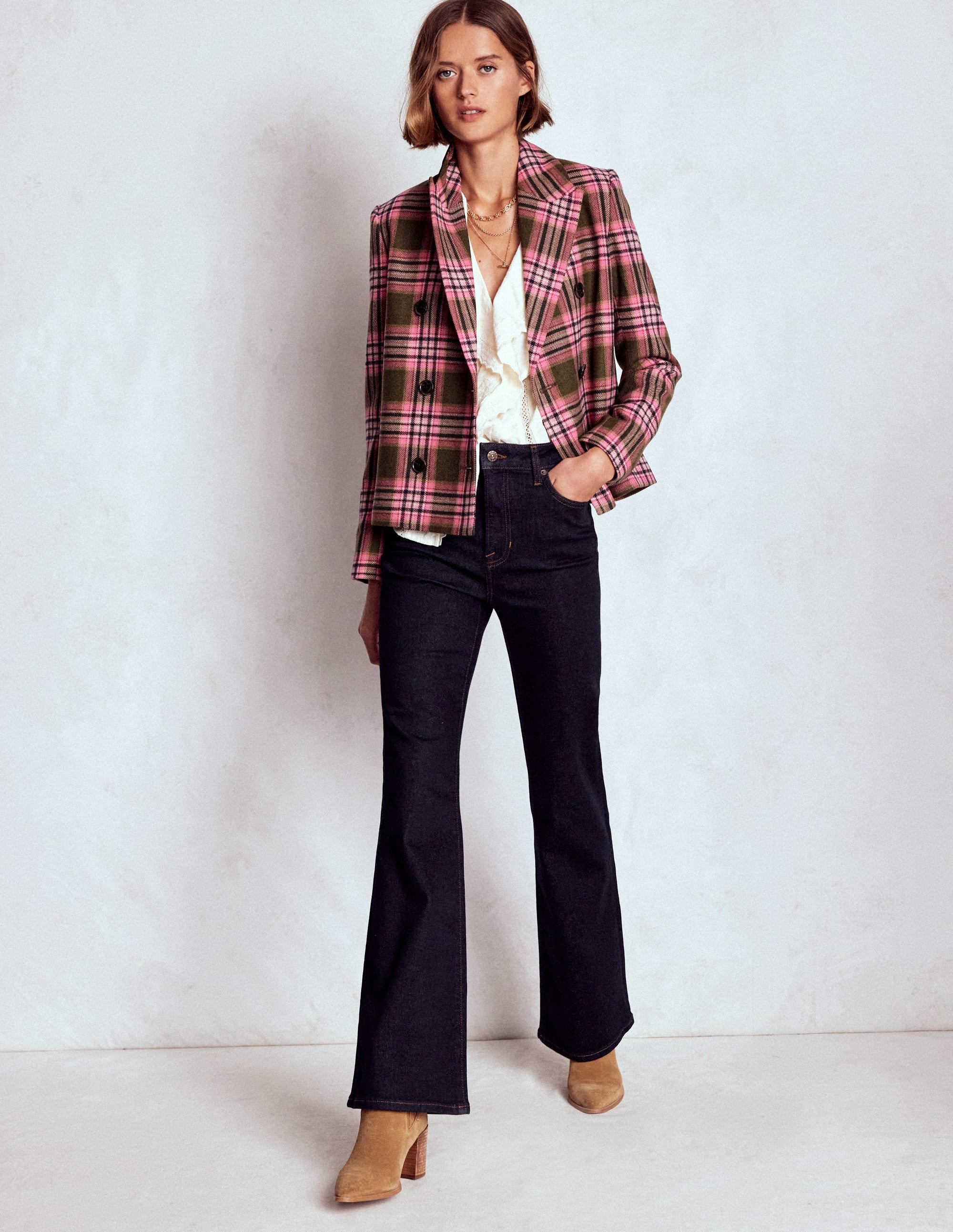 A woman wearing indigo high-rise fitted flare jeans, paired with a plaid blazer and beige boots.