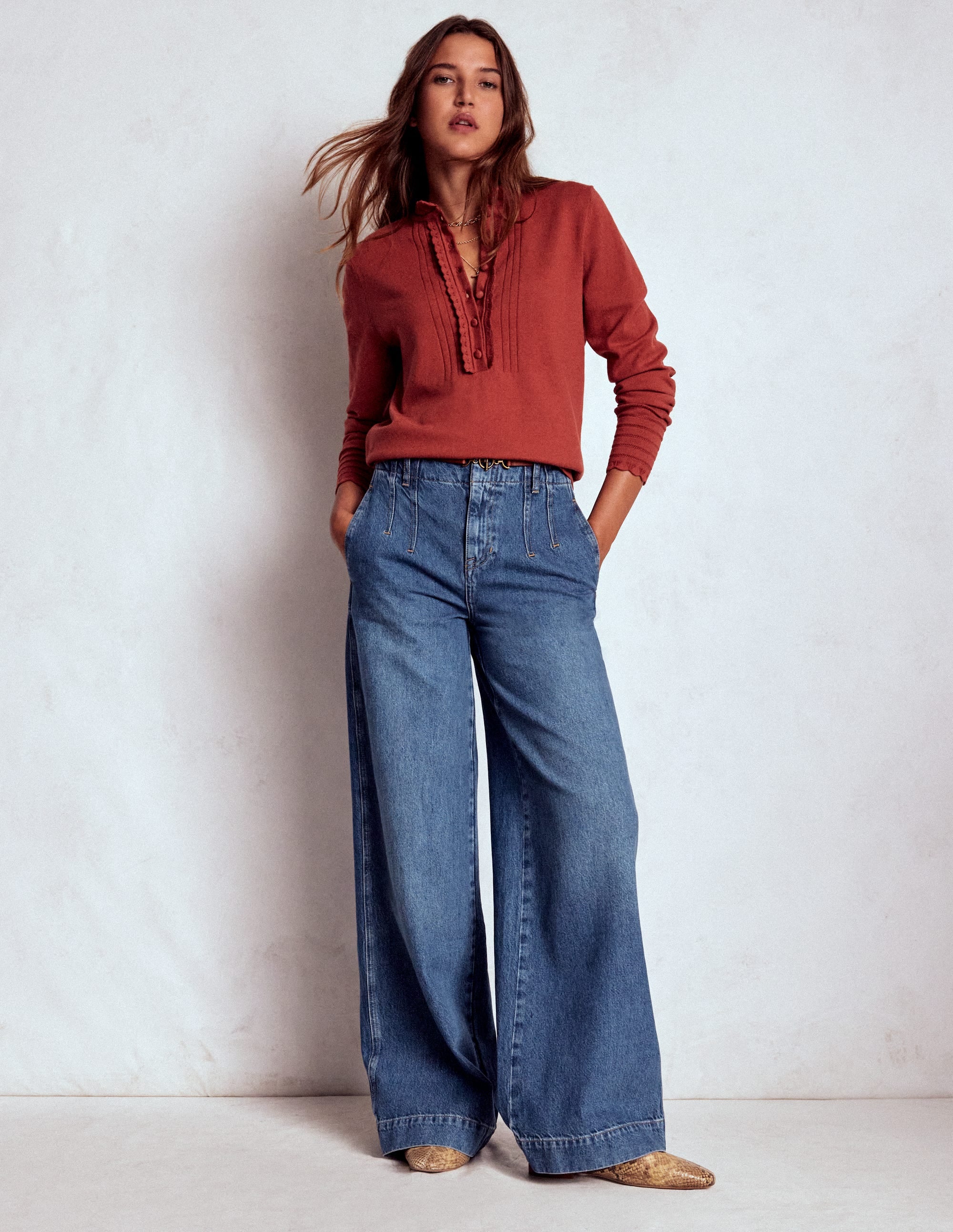 A woman wearing mid vintage blue wide-leg jeans with high waist and exposed stitch detail, paired with a rust-colored top.
