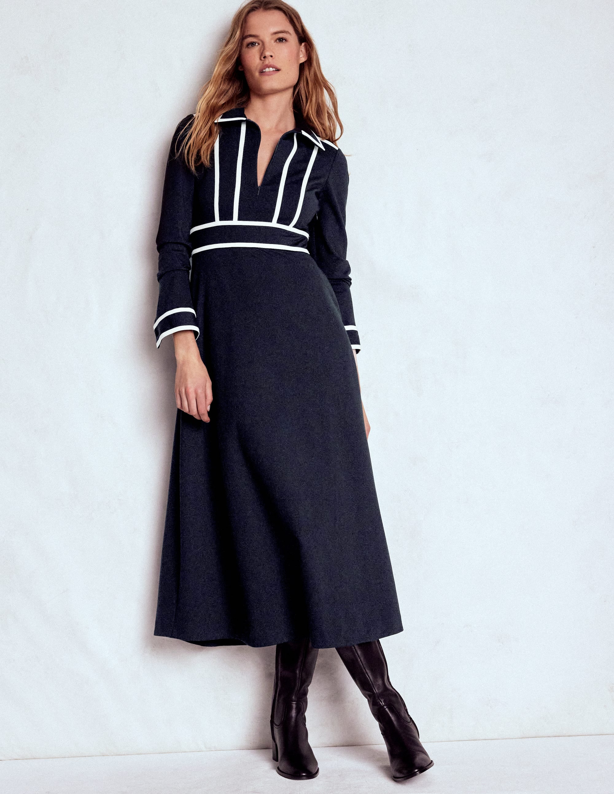 A woman wearing a navy contrast ponte midi dress with white detailing, long sleeves, and black boots.