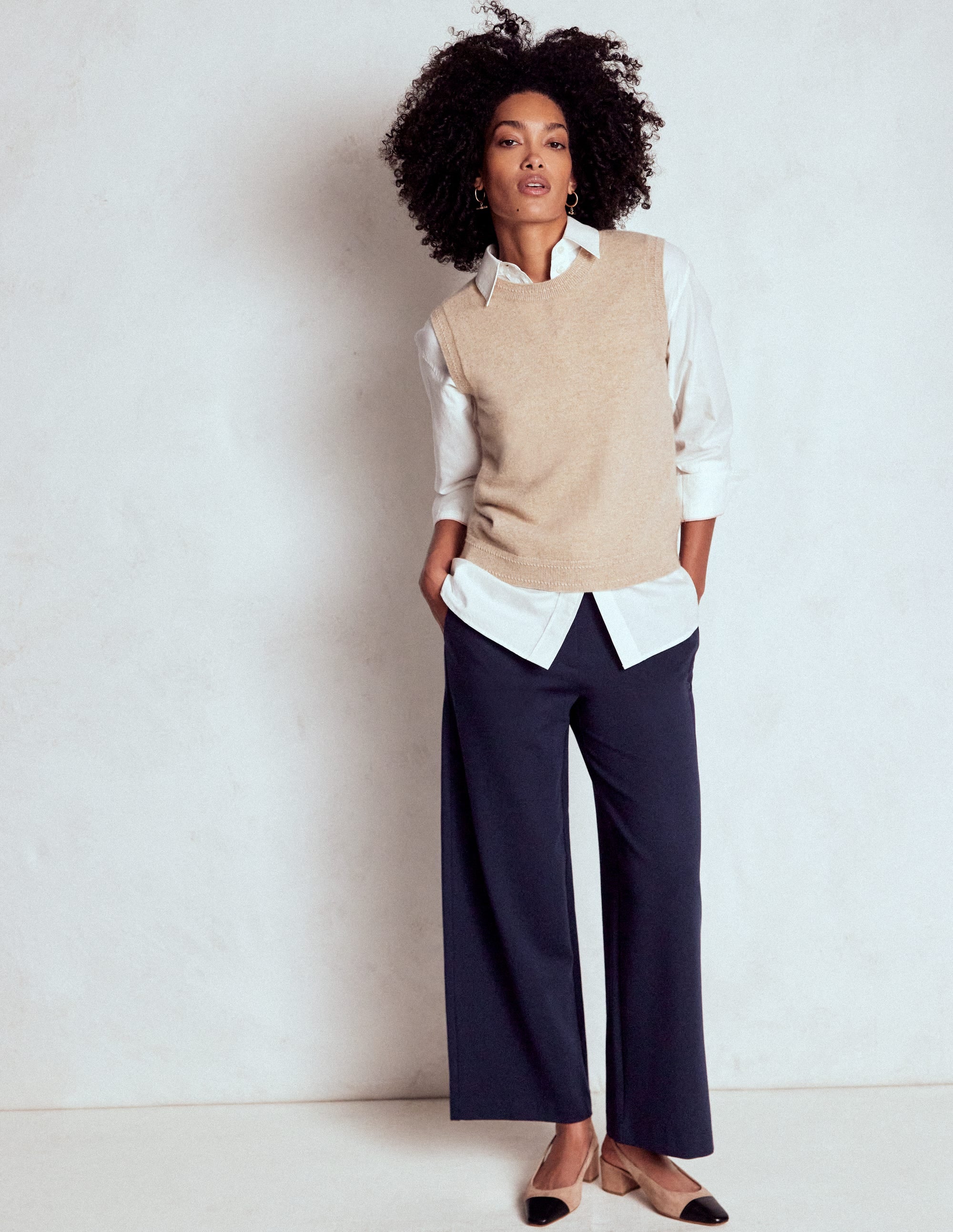 A woman wearing navy crop trousers with a high waist, paired with a white shirt and beige heels.