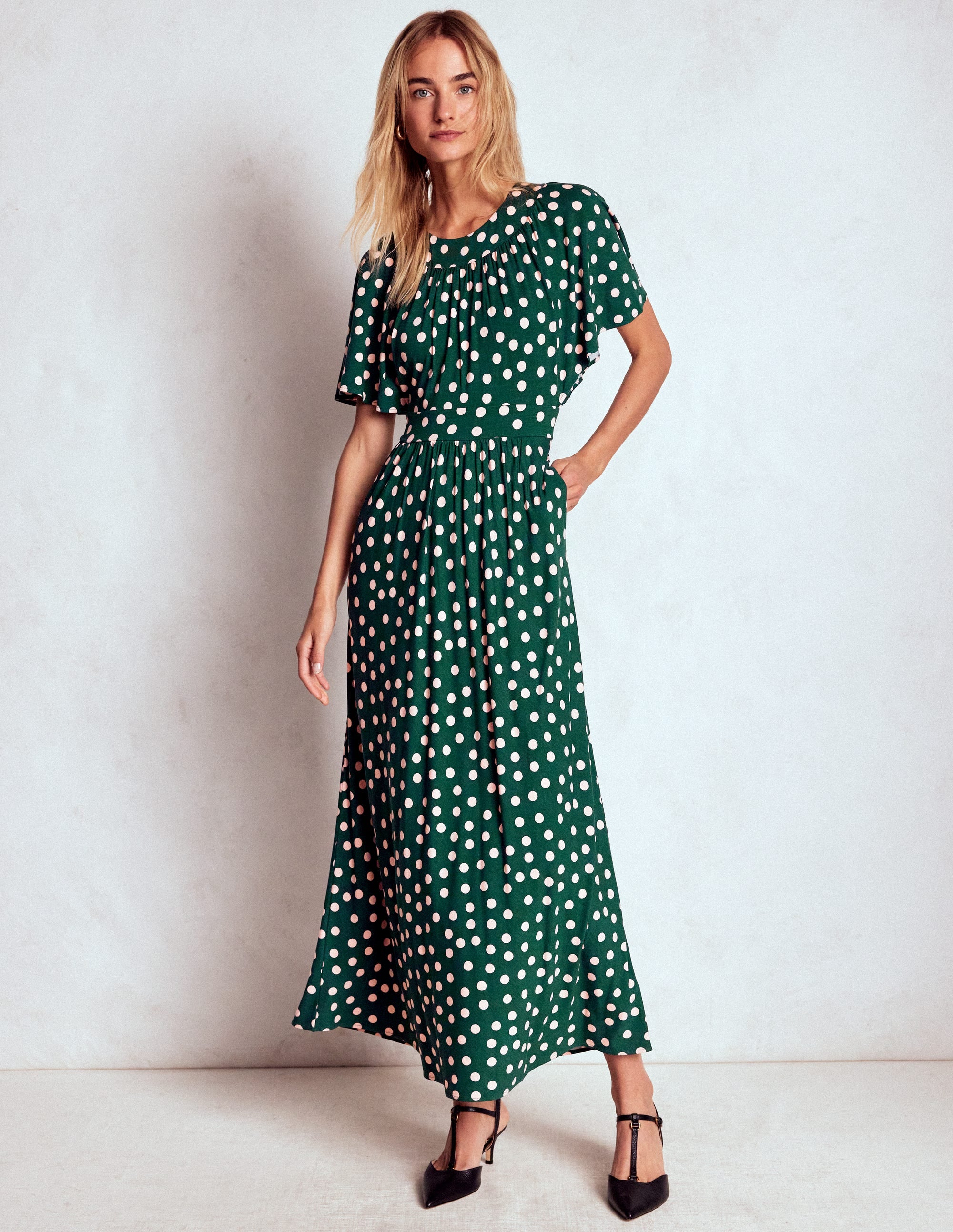 A woman wearing a green maxi dress with white painted dots, flutter sleeves, and a bias-cut skirt.