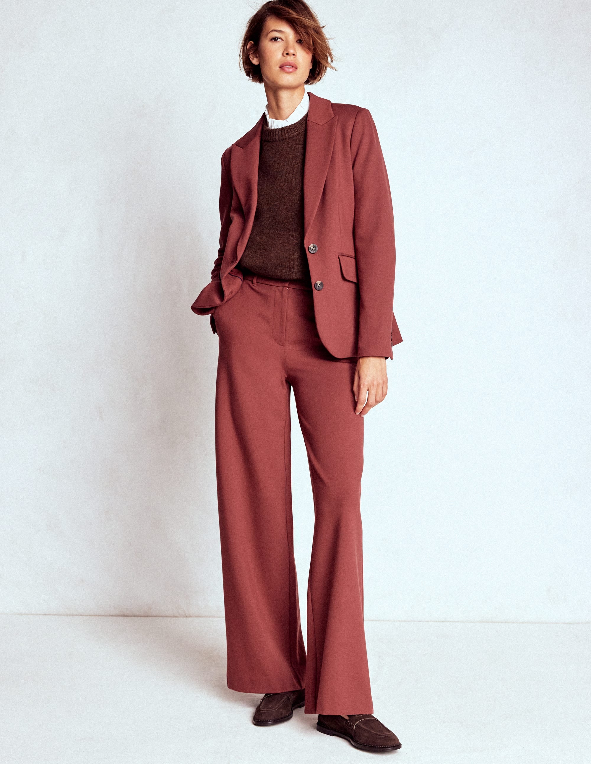 A woman wearing a chestnut-colored blazer with a button front, paired with matching trousers and a brown sweater.