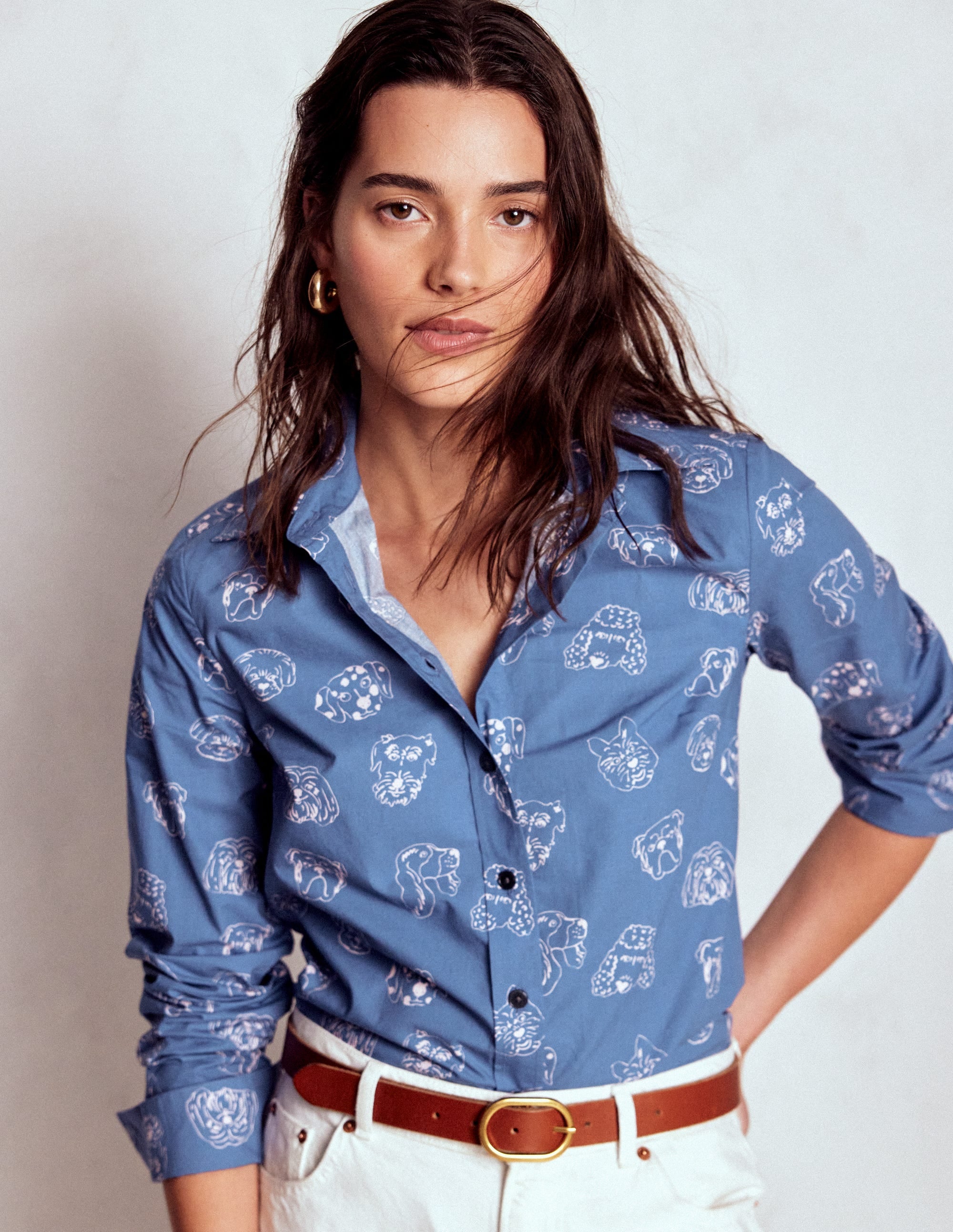 A woman wearing a blue cotton shirt with a multi-dog print, long sleeves, and a collar.