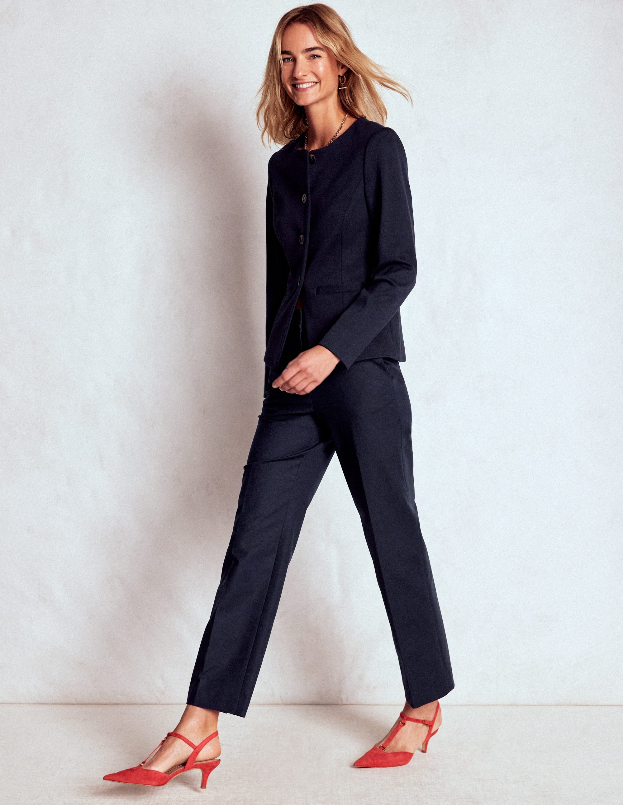 A woman wearing navy tailored 7/8 trousers with a matching navy blazer, standing against a plain background.