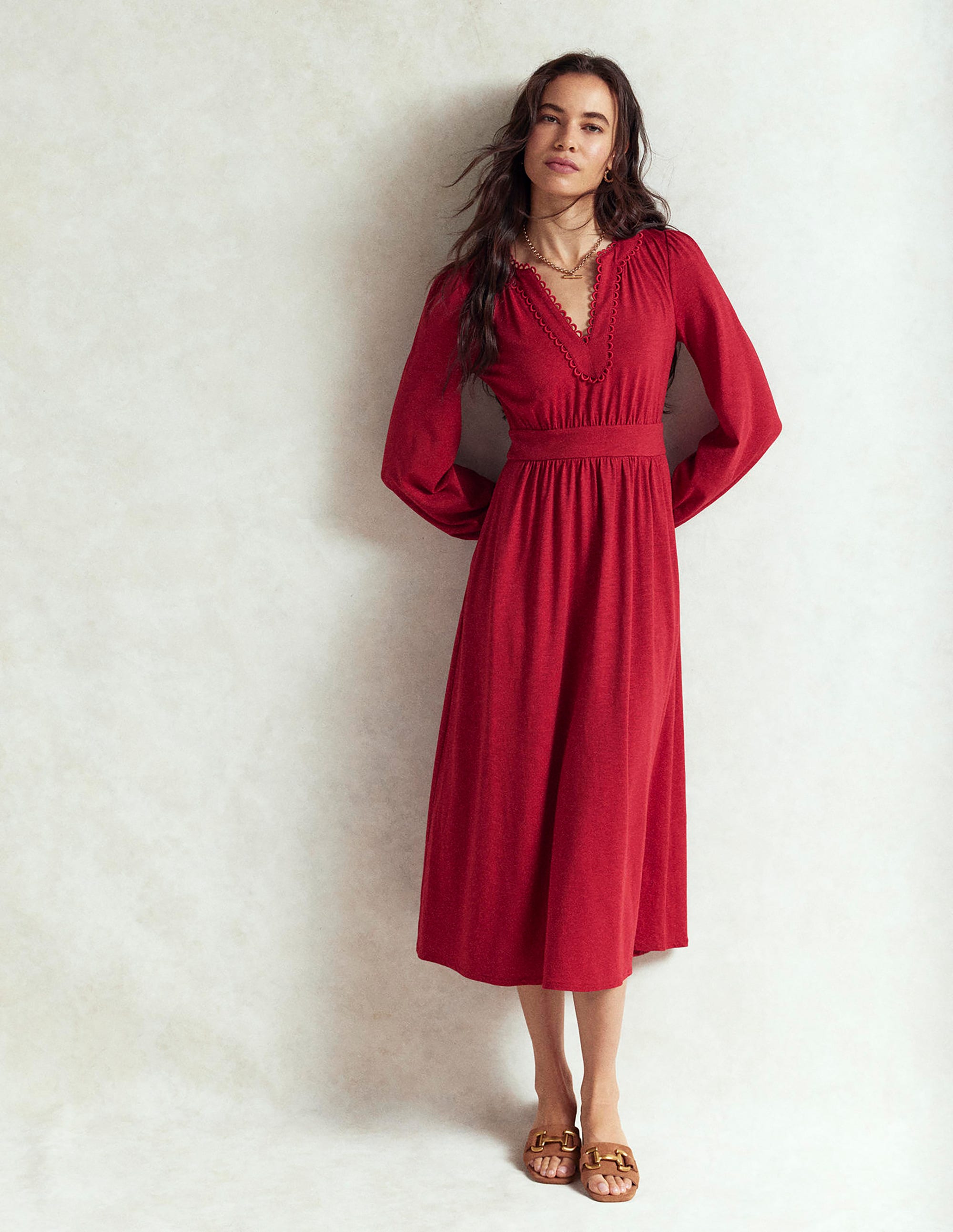 A woman wearing a Carmine Red midi dress with blouson sleeves, a picot trim on the V-neckline, and side seam pockets.