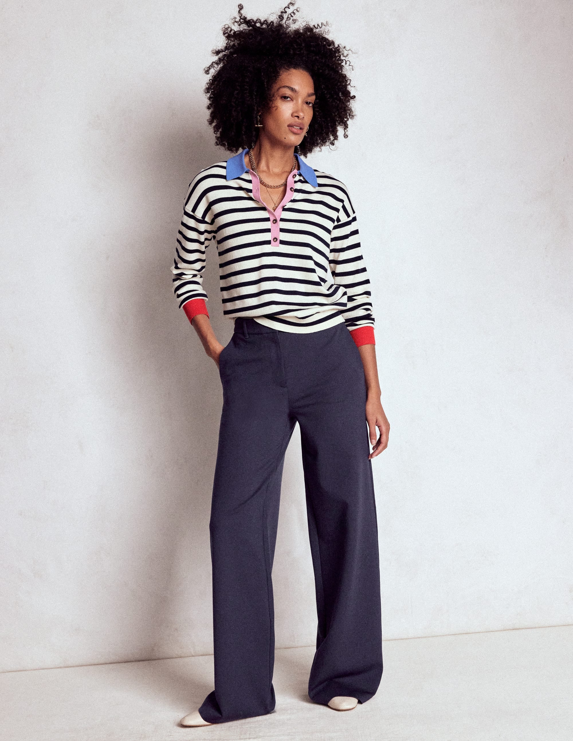 A woman wearing navy Belgravia Ponte Trousers with a subtle flare, paired with a striped top with blue, pink, and red accents.